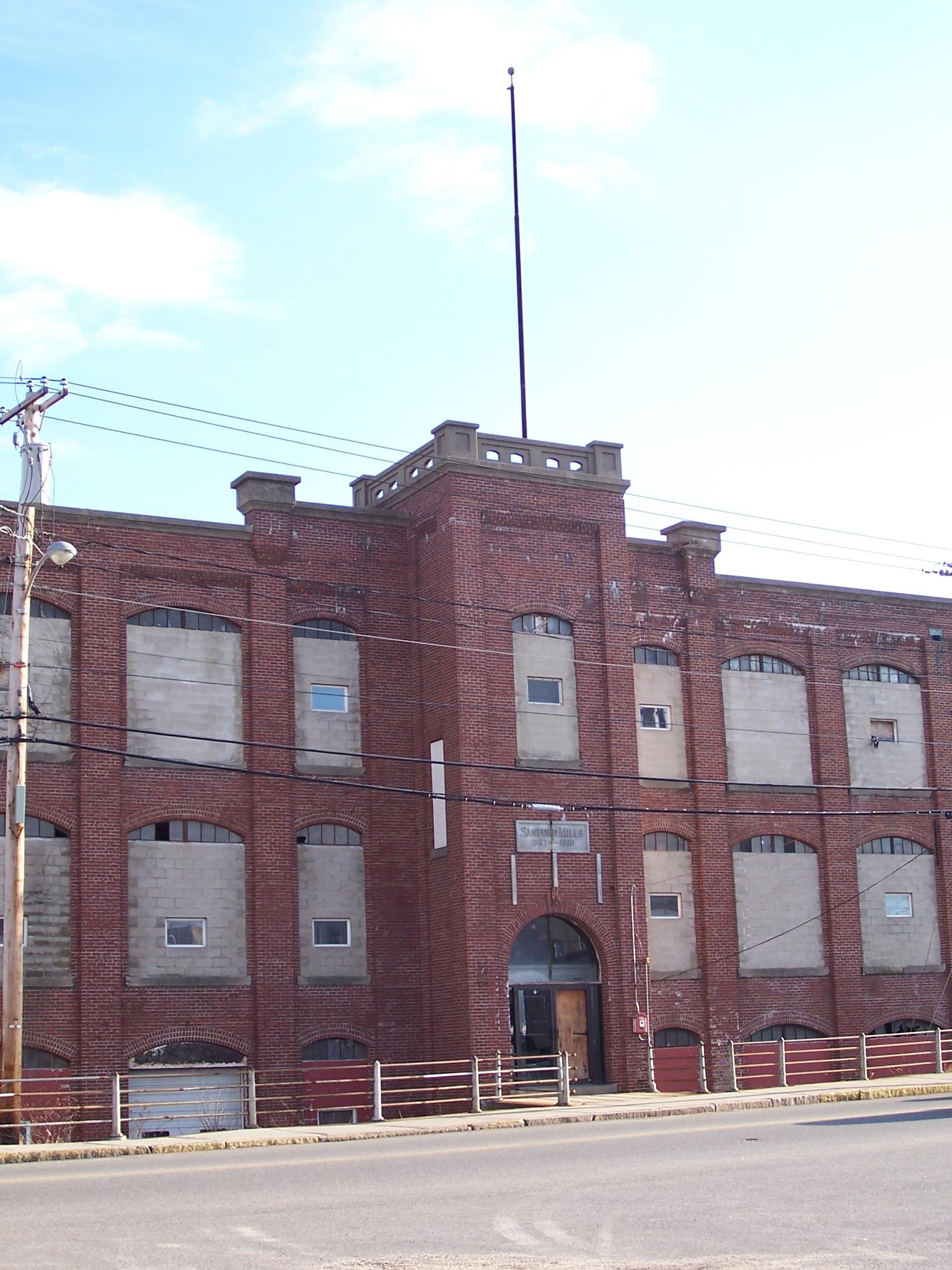 Large old brick building with boarded windows under a bright sky.