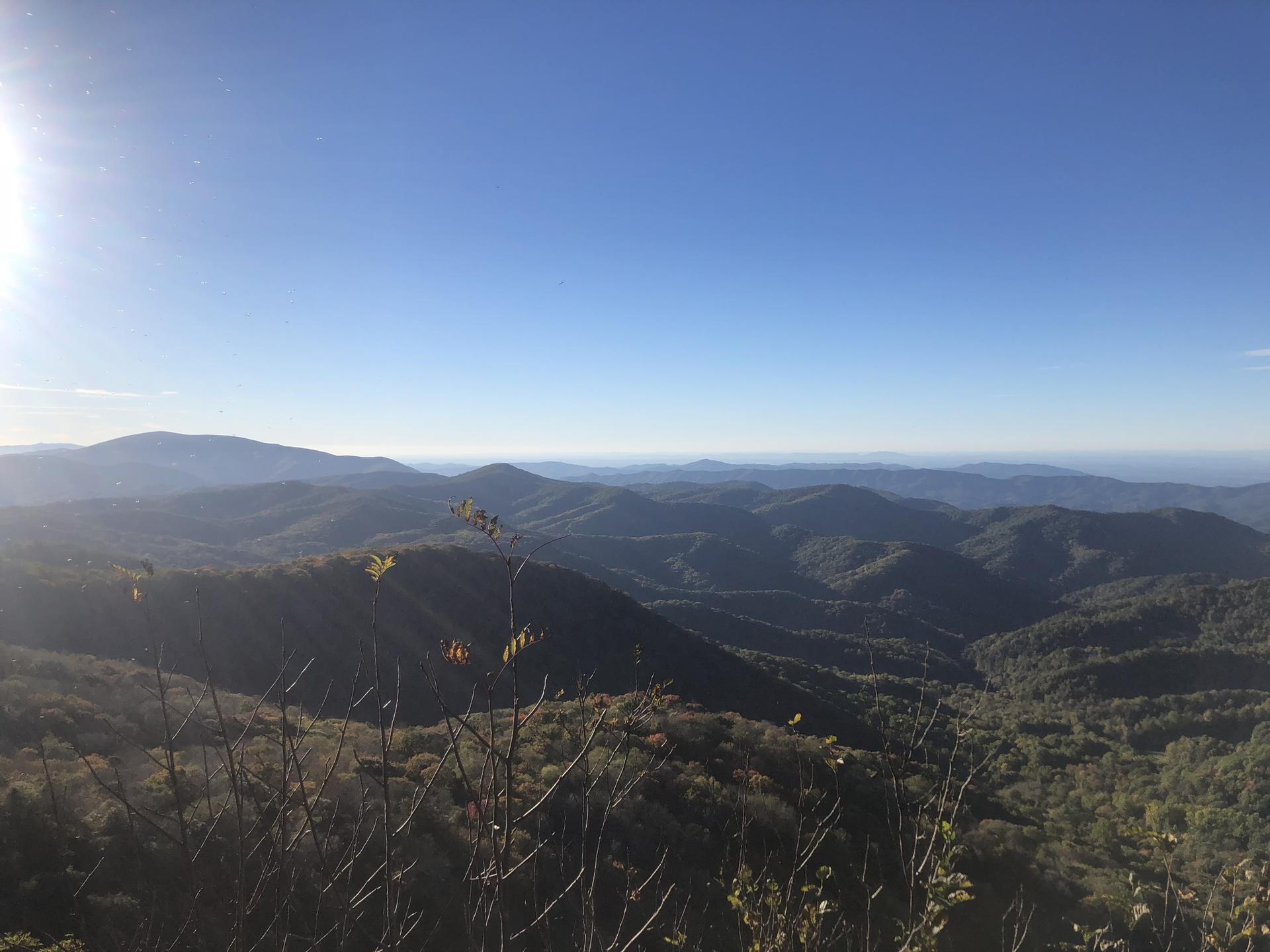 Sun shines over rolling, forested mountains stretching to the hazy horizon.