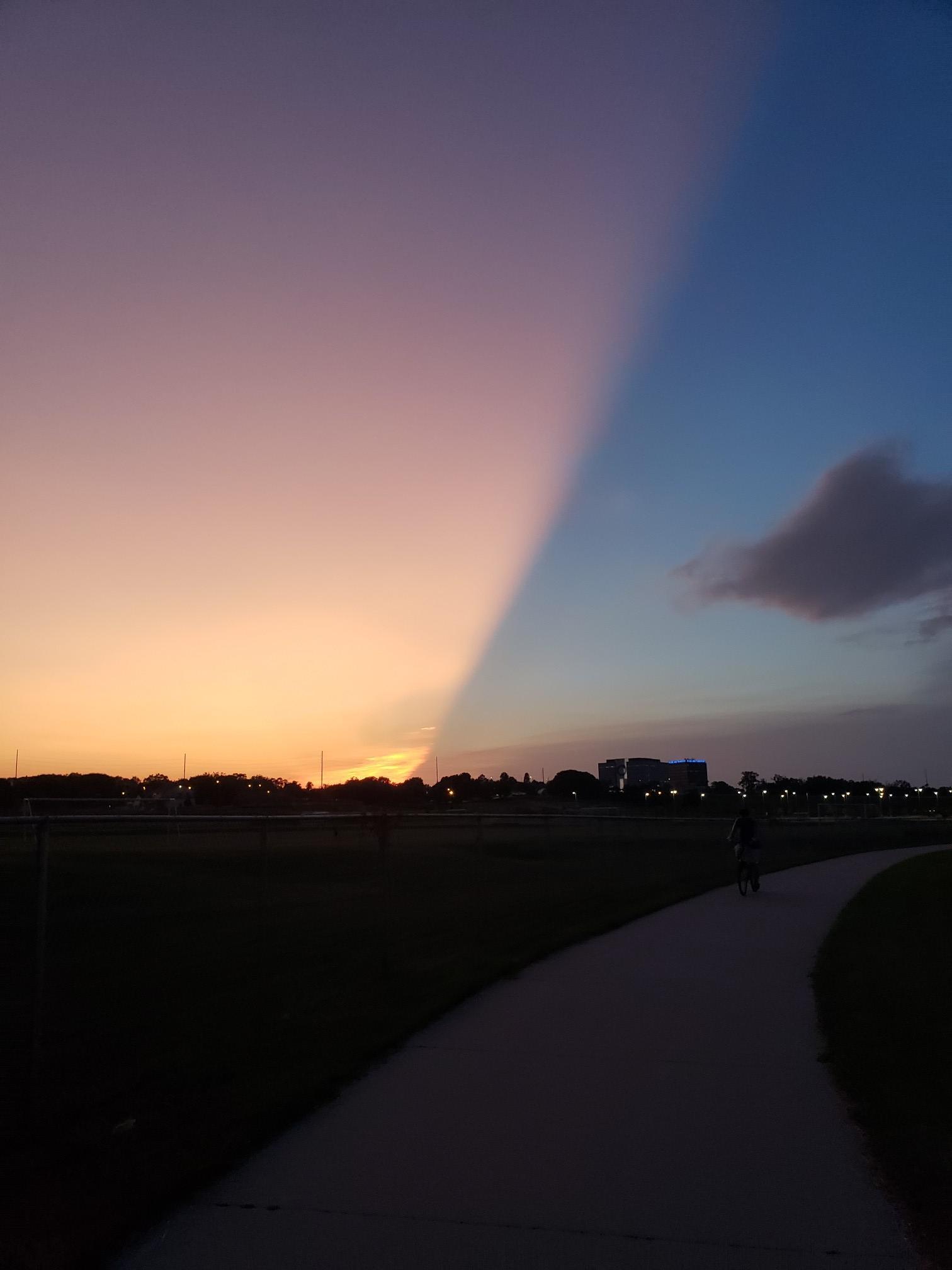 Sunset sky split by a dramatic shadow over a path and field.