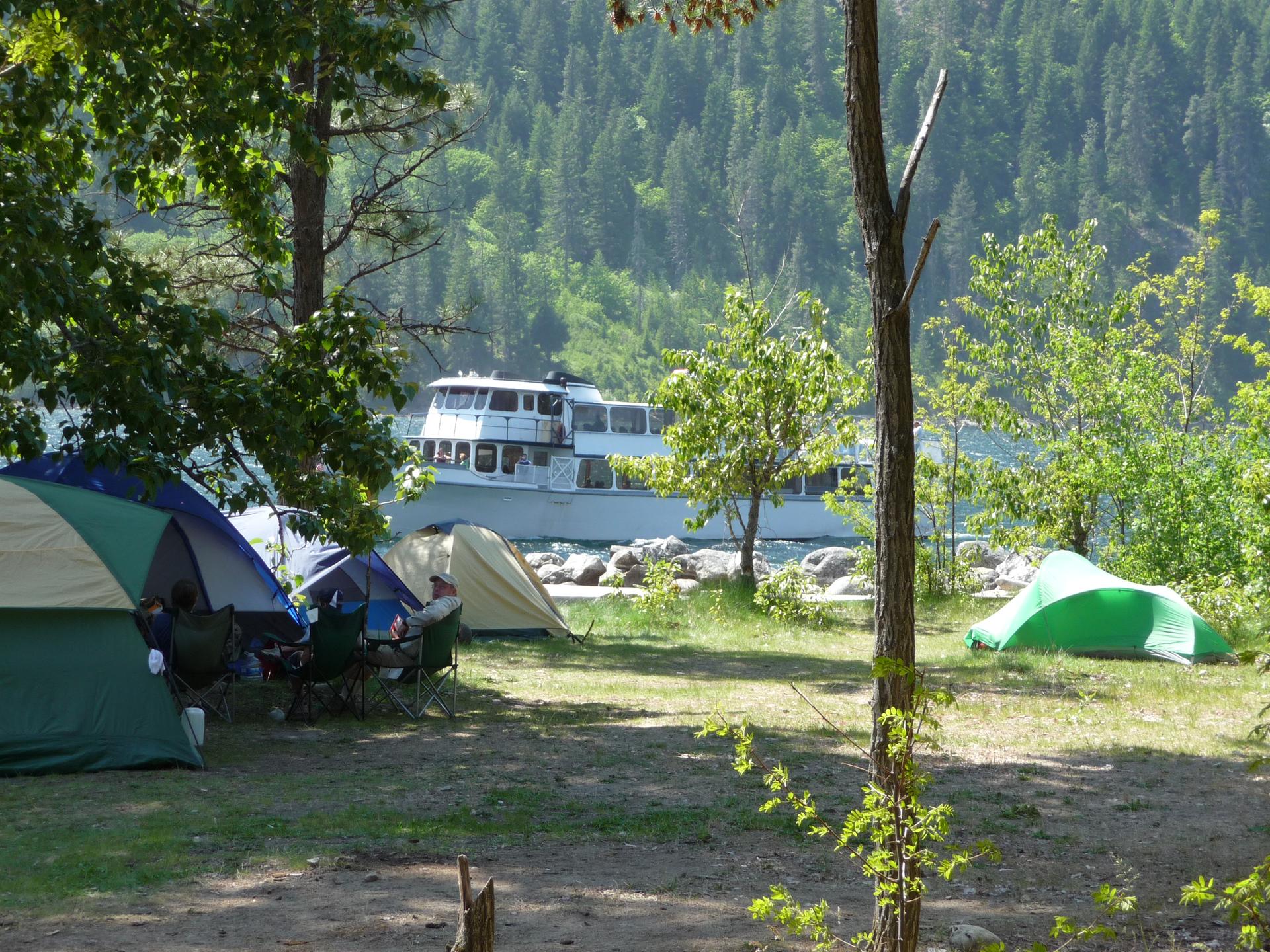 Tents set up by a lake with a large passenger boat in the background.