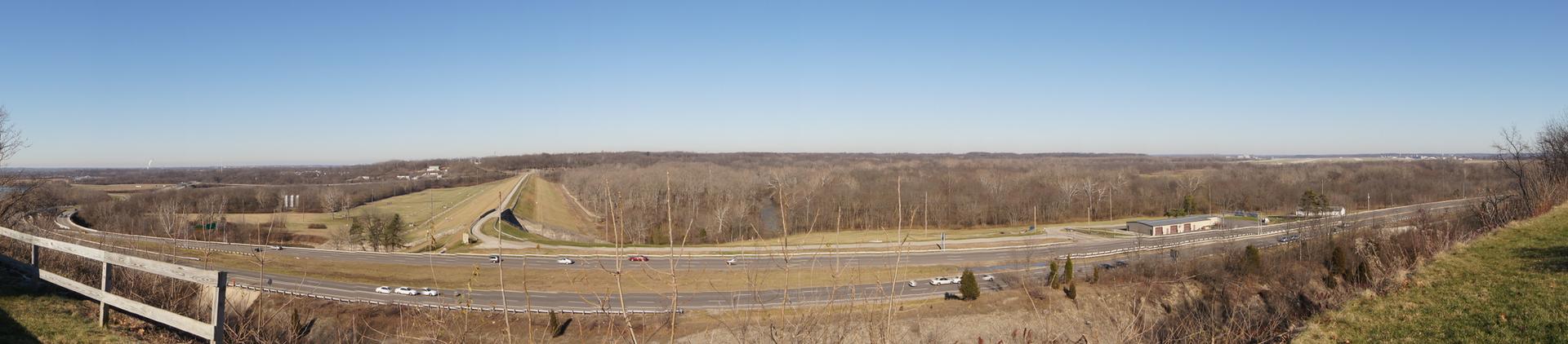 Panoramic view of a highway winding through a valley with bare trees under clear sky.