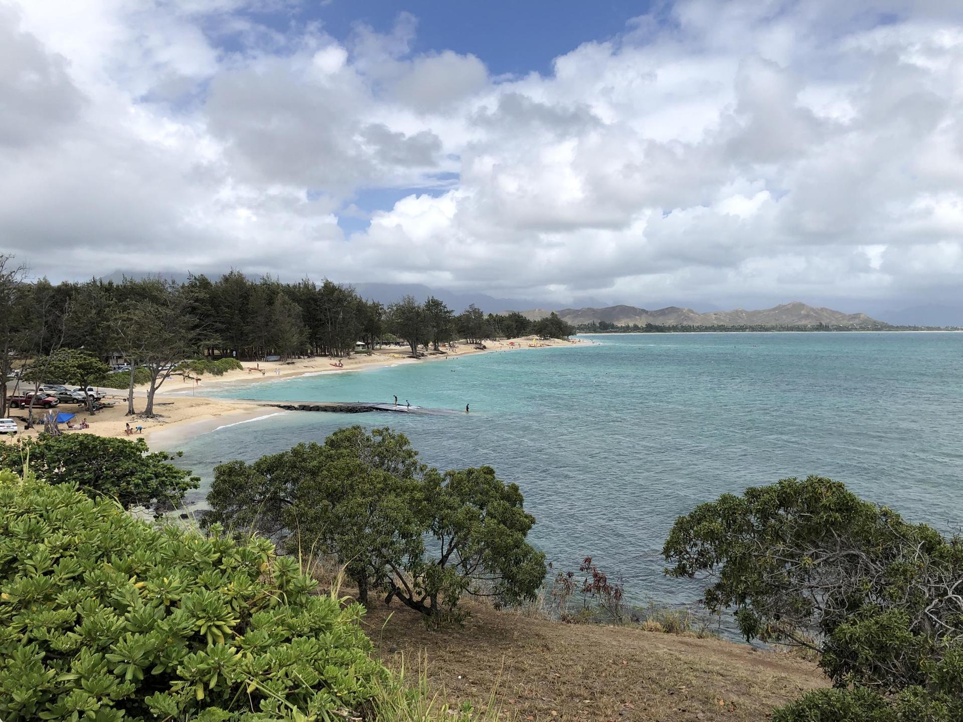 Panoramic view of a long sandy beach, turquoise ocean, and distant mountains.