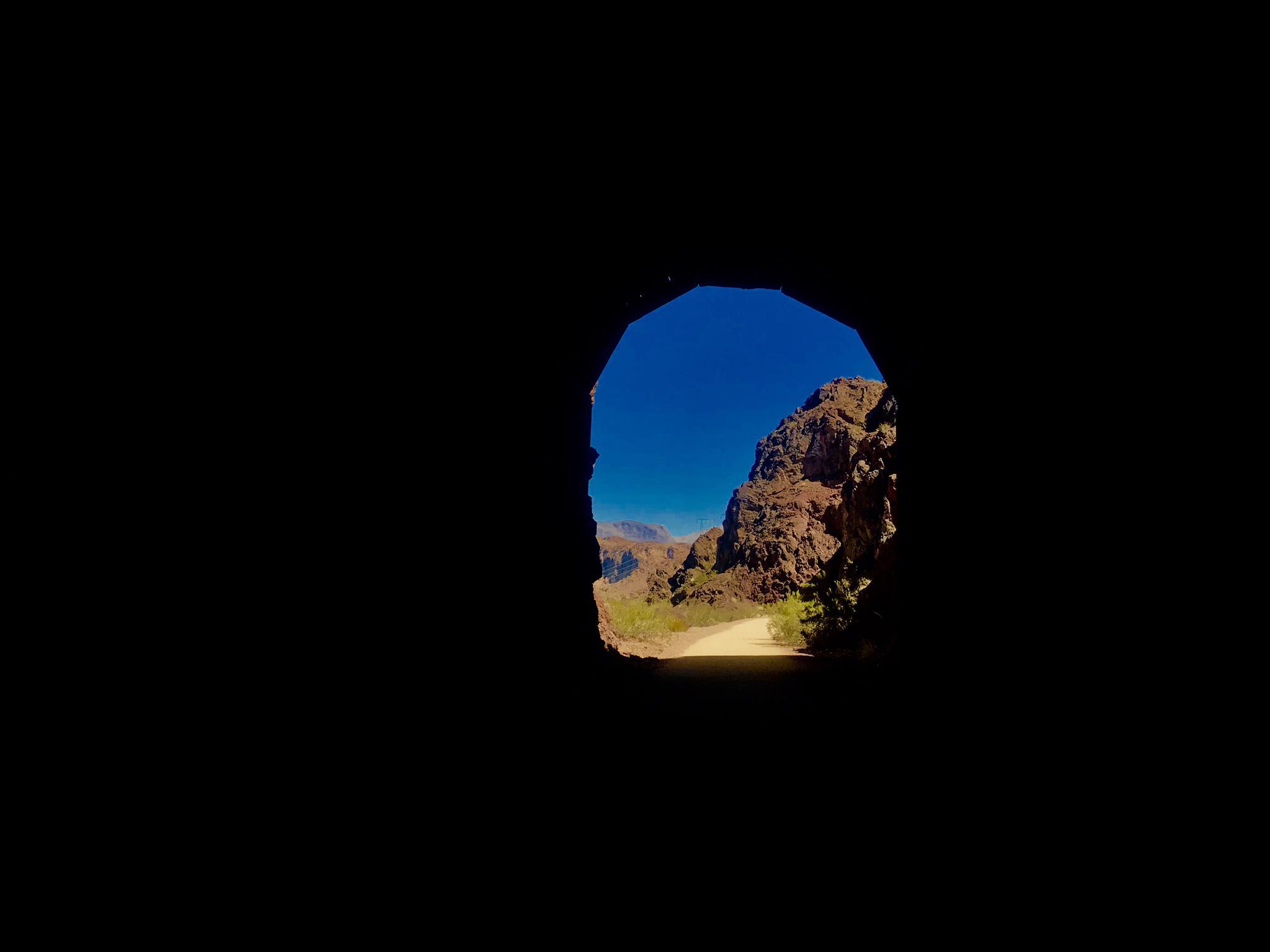 View from a dark tunnel opening to bright desert mountains and sky.