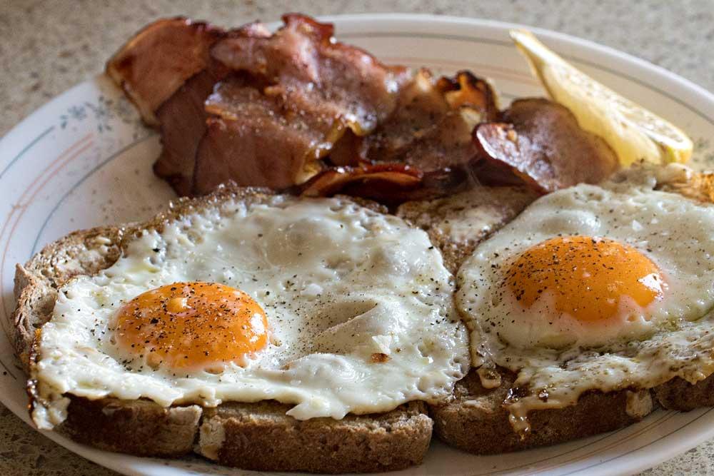 Close-up of two fried eggs on toast with bacon and lemon on a plate.