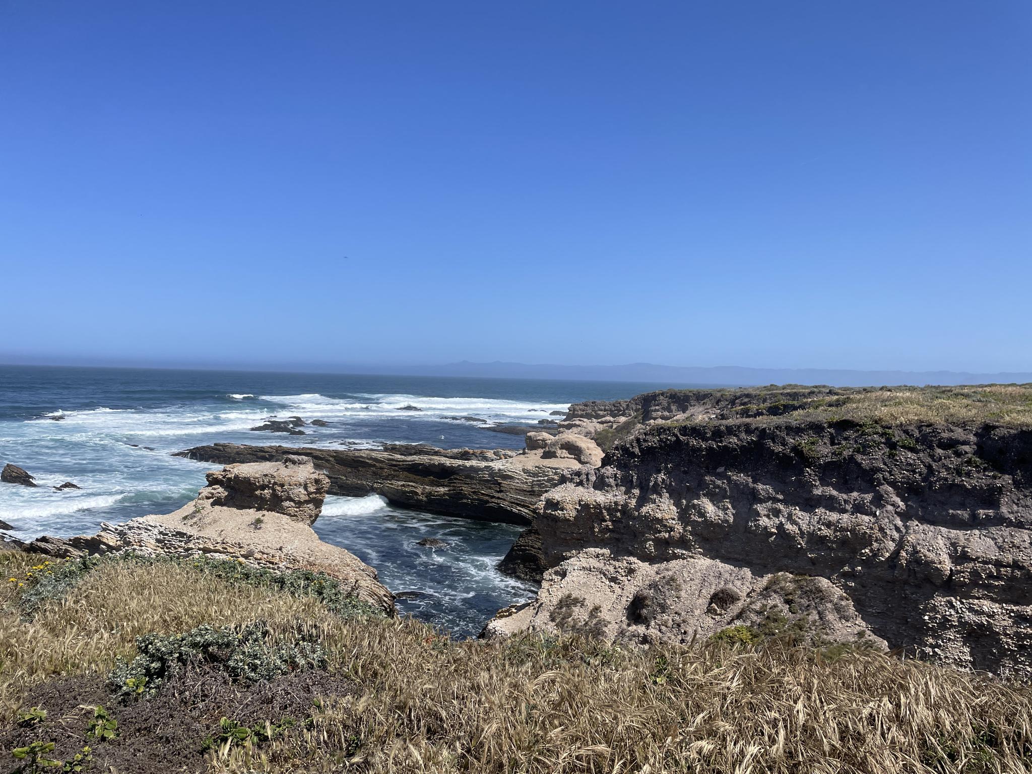 Sunny view of rugged coastal cliffs and ocean with waves.