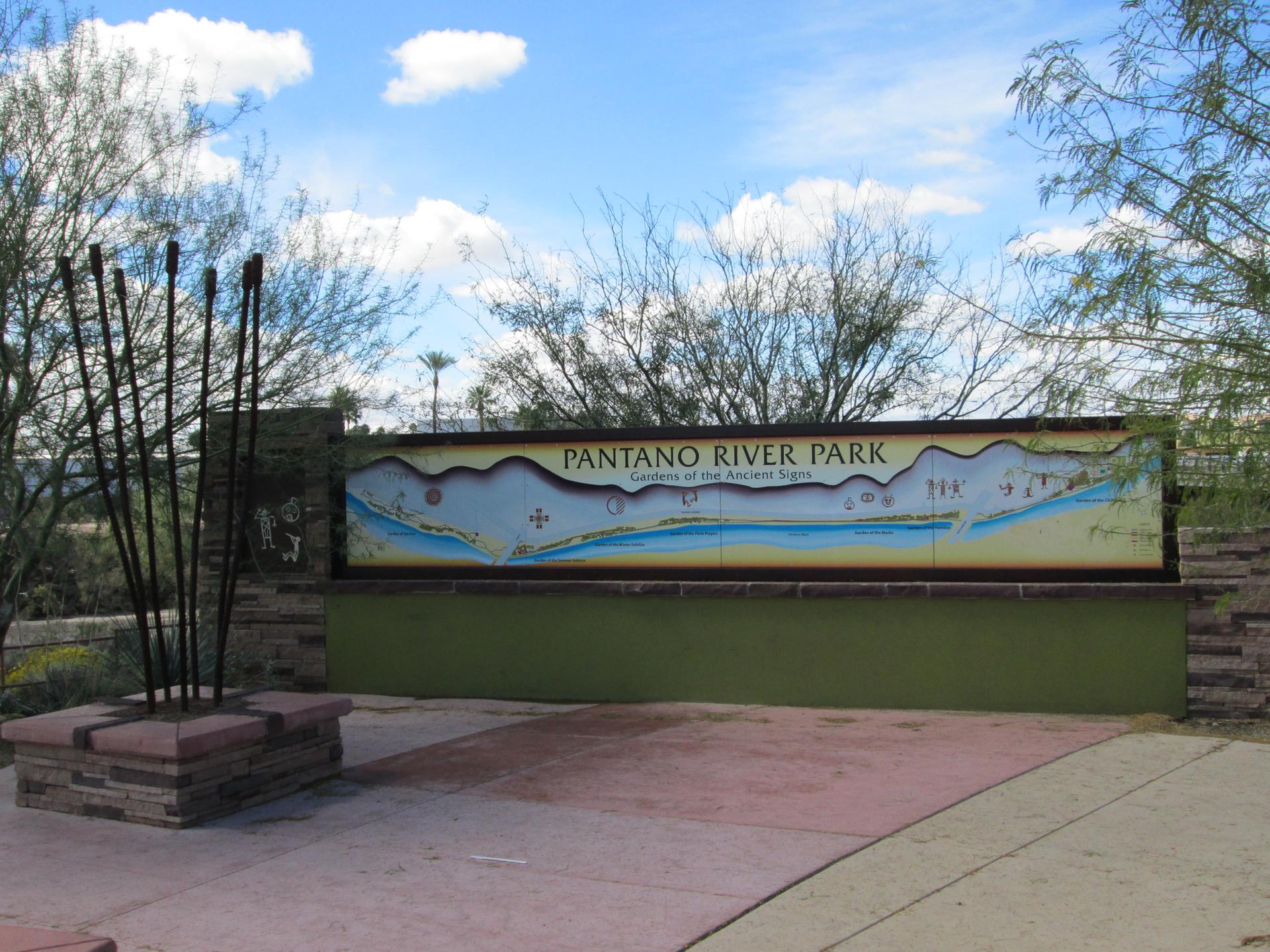 Park sign with a map, surrounded by desert trees under a blue sky.