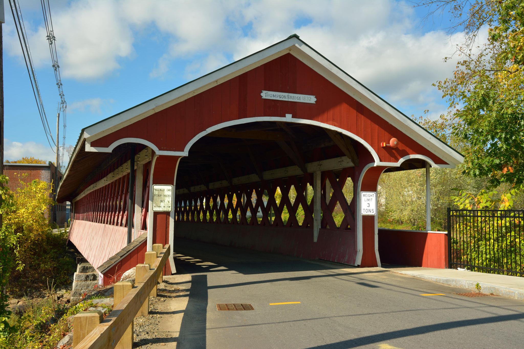 A red covered bridge with diamond windows under a bright blue sky. - Ashuelot Rail Trail Loop