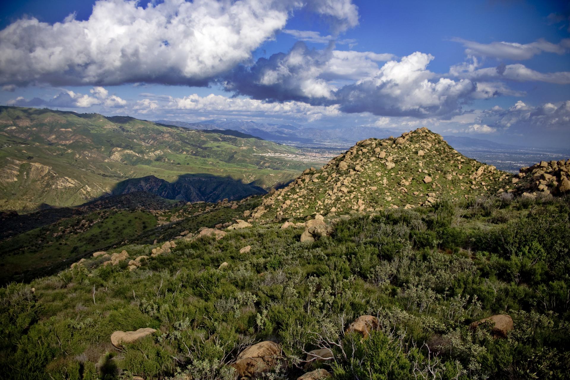 Rocky green hills under a partly cloudy sky with distant valley views.