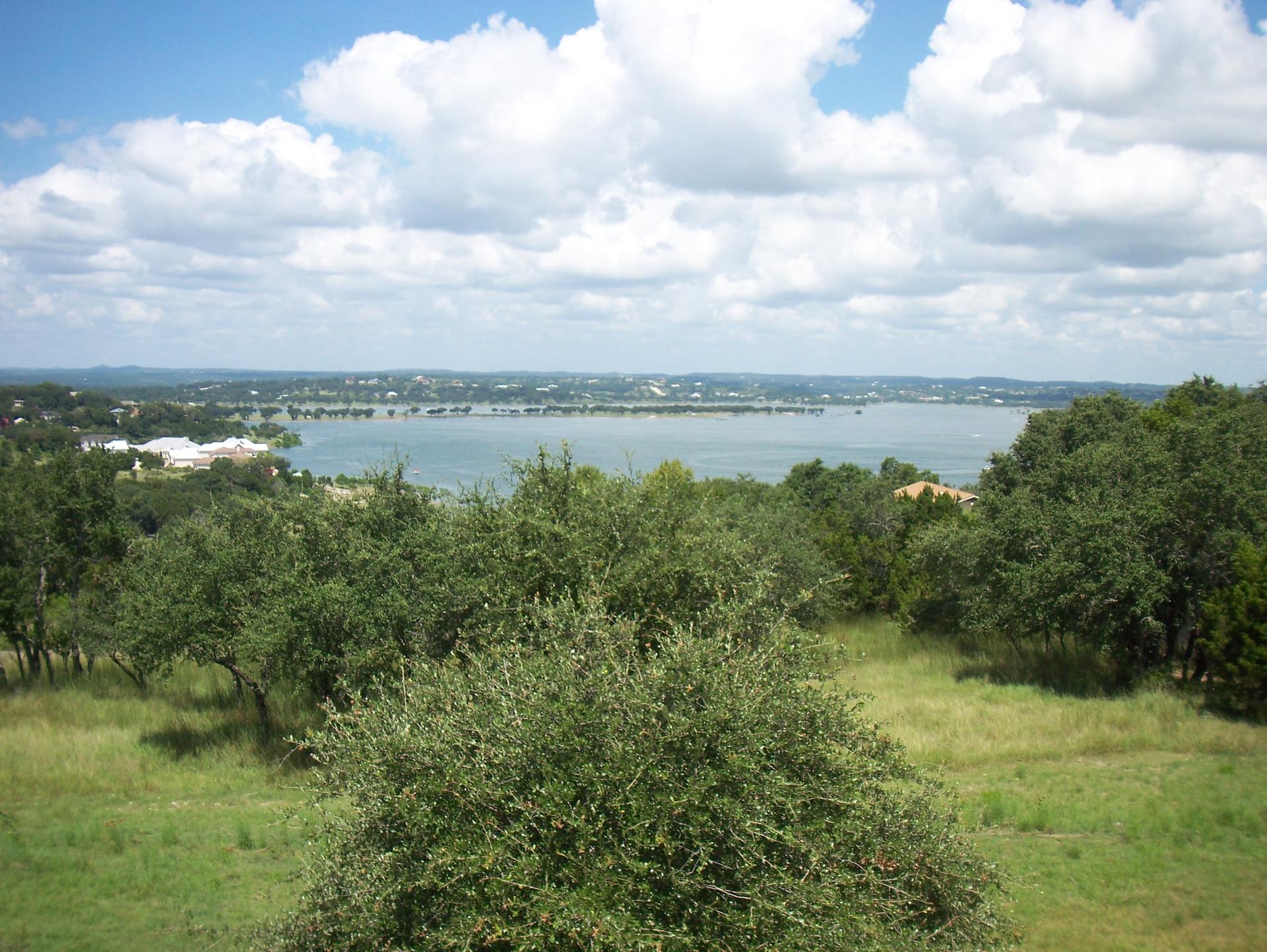 Panoramic view of a large lake surrounded by green trees under a partly cloudy sky.