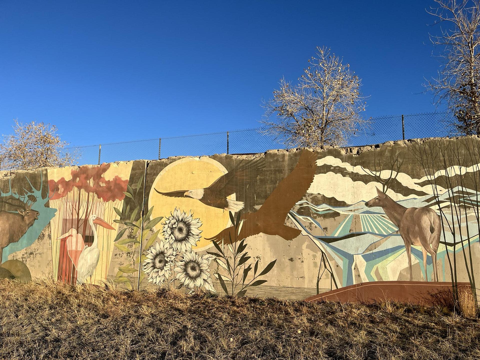 Colorful mural depicting wildlife and nature scenes on a wall under a blue sky.