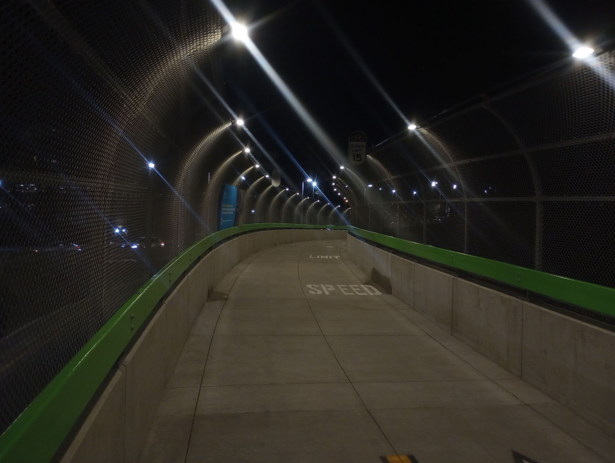 Curved pedestrian path inside a brightly lit mesh tunnel at night. - NorthWalk