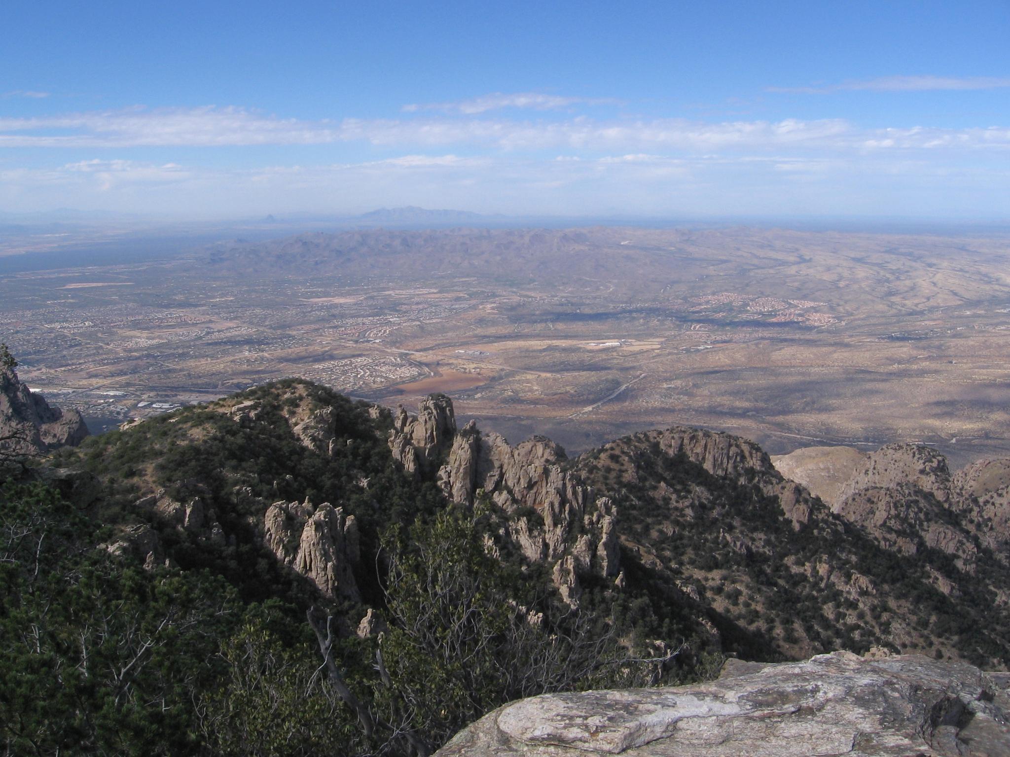 Expansive desert valley and distant mountains seen from a rocky mountain peak.