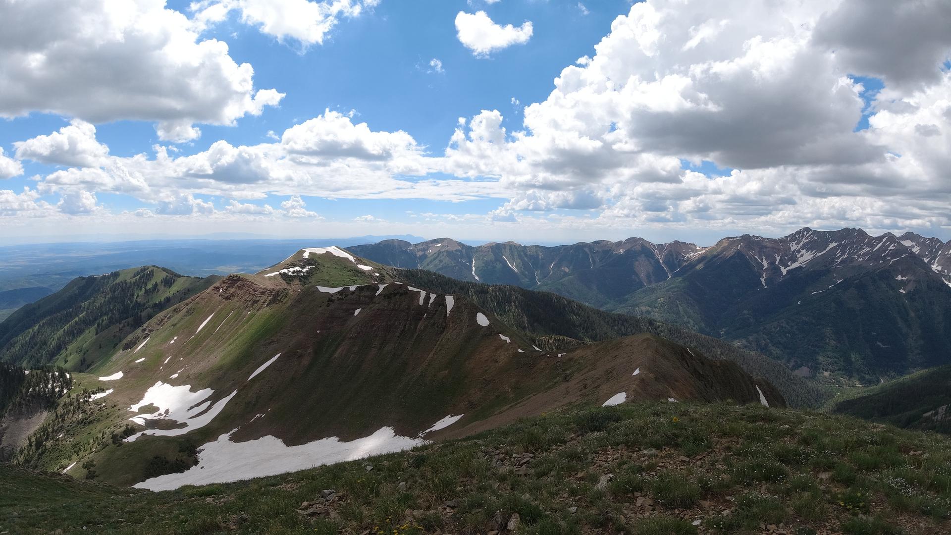 Panoramic view of a rugged mountain range with snow patches under a cloudy sky.
