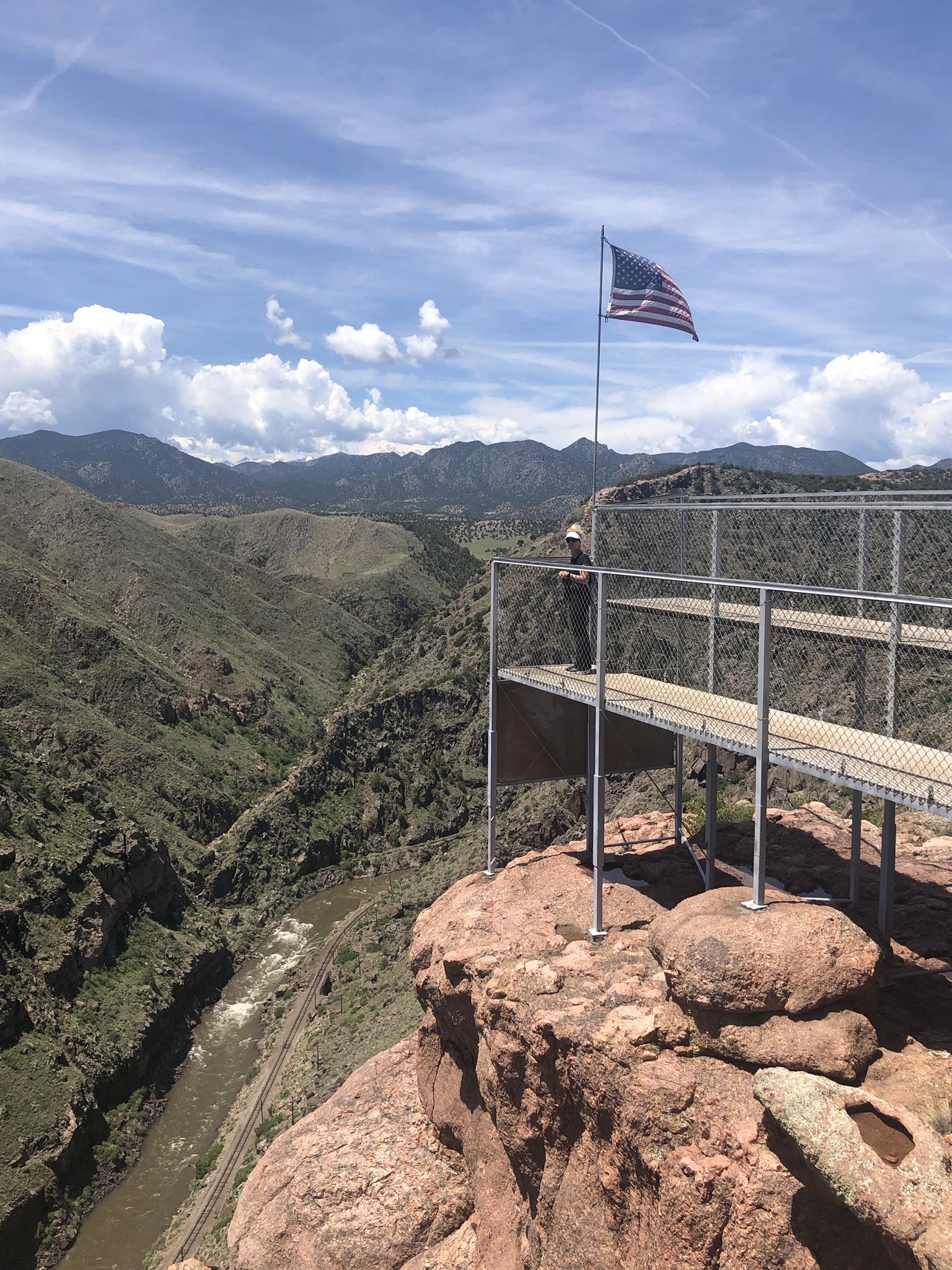 Person on a viewing platform with an American flag overlooking a deep canyon.
