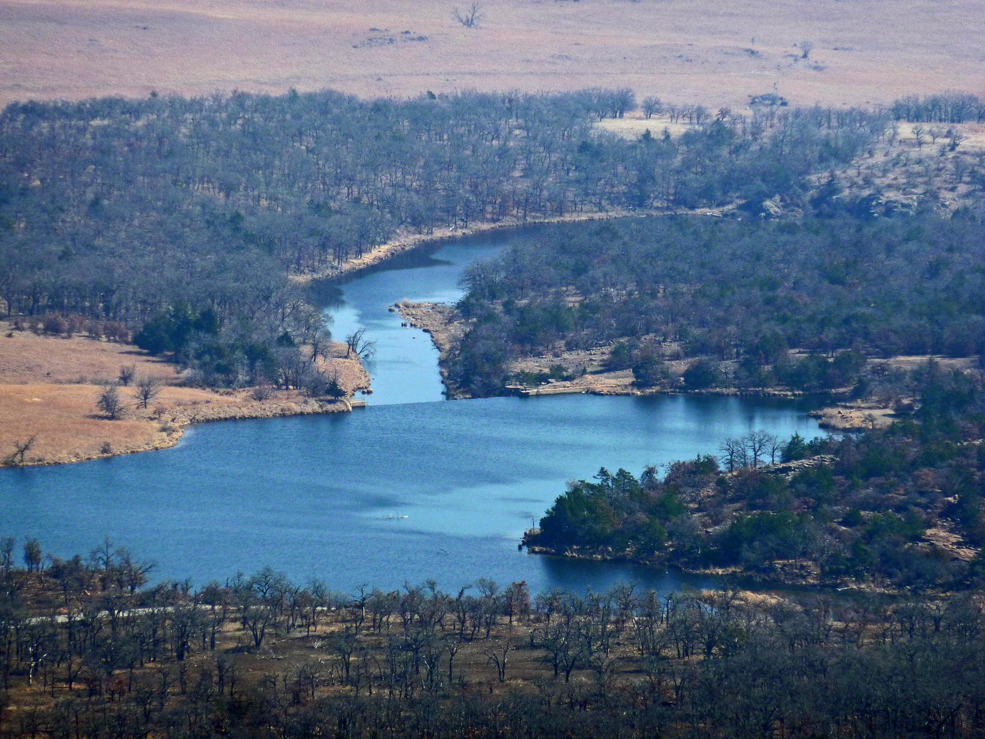 Aerial view of a winding blue river surrounded by bare trees and dry land.
