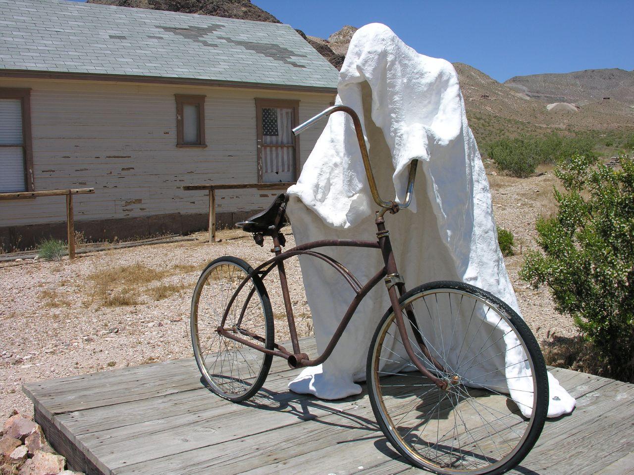 White draped figure with an old bicycle on a wooden porch.