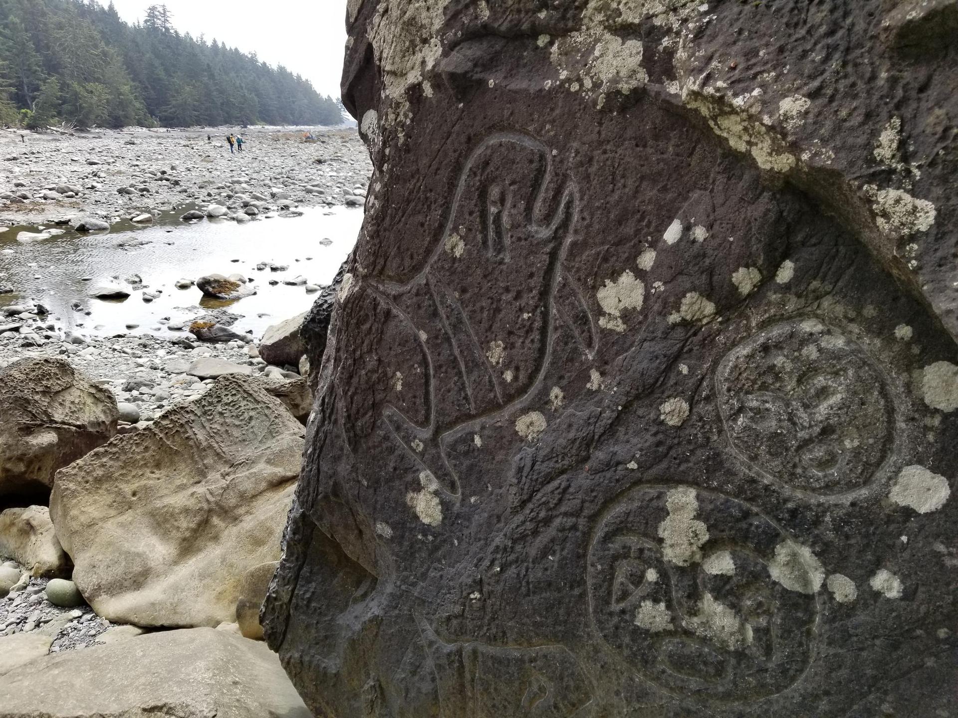 Ancient carvings on a large rock beside a rocky riverbed.