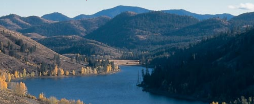 A winding lake surrounded by forested hills with autumn trees under clear skies.