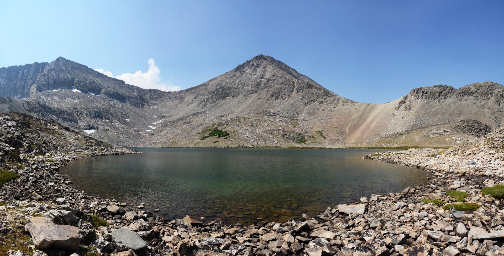Clear alpine lake surrounded by rocky mountains under a bright blue sky.