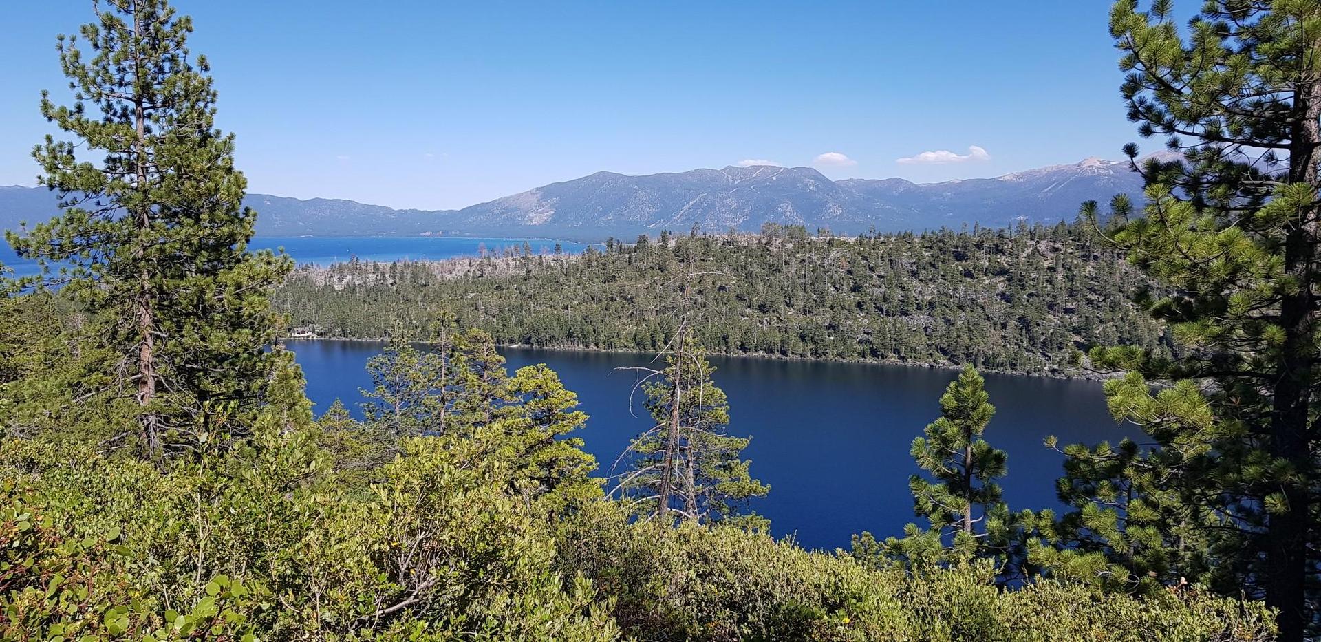 Sunny view of a deep blue lake surrounded by green forests and mountains.