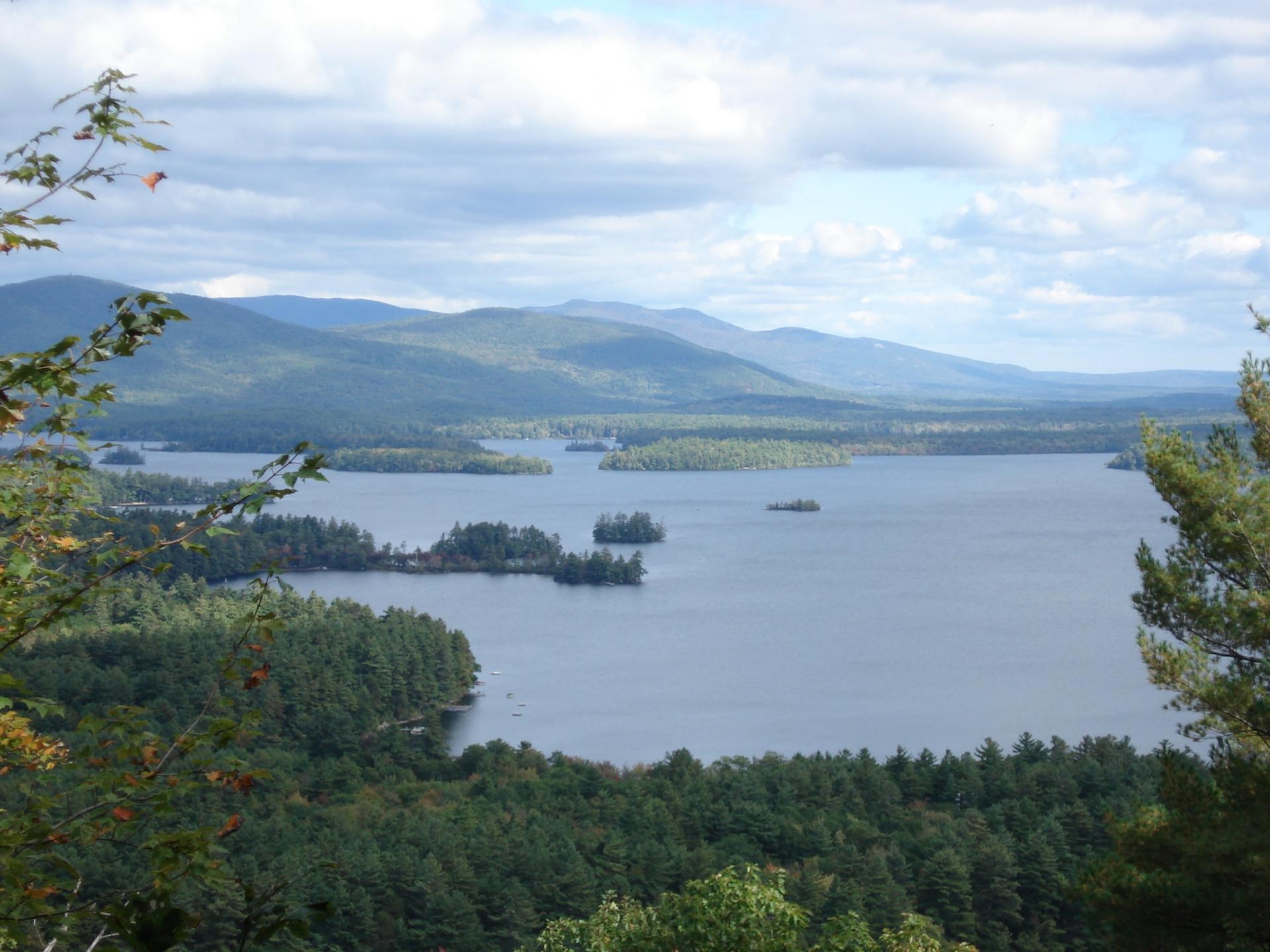 Panoramic view of a large lake with islands, surrounded by forests and mountains.