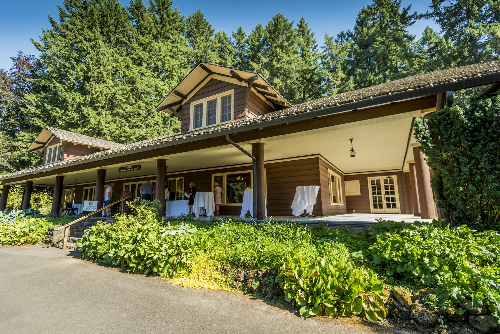 Sunny day illuminates a rustic lodge with a wide porch and people gathered.