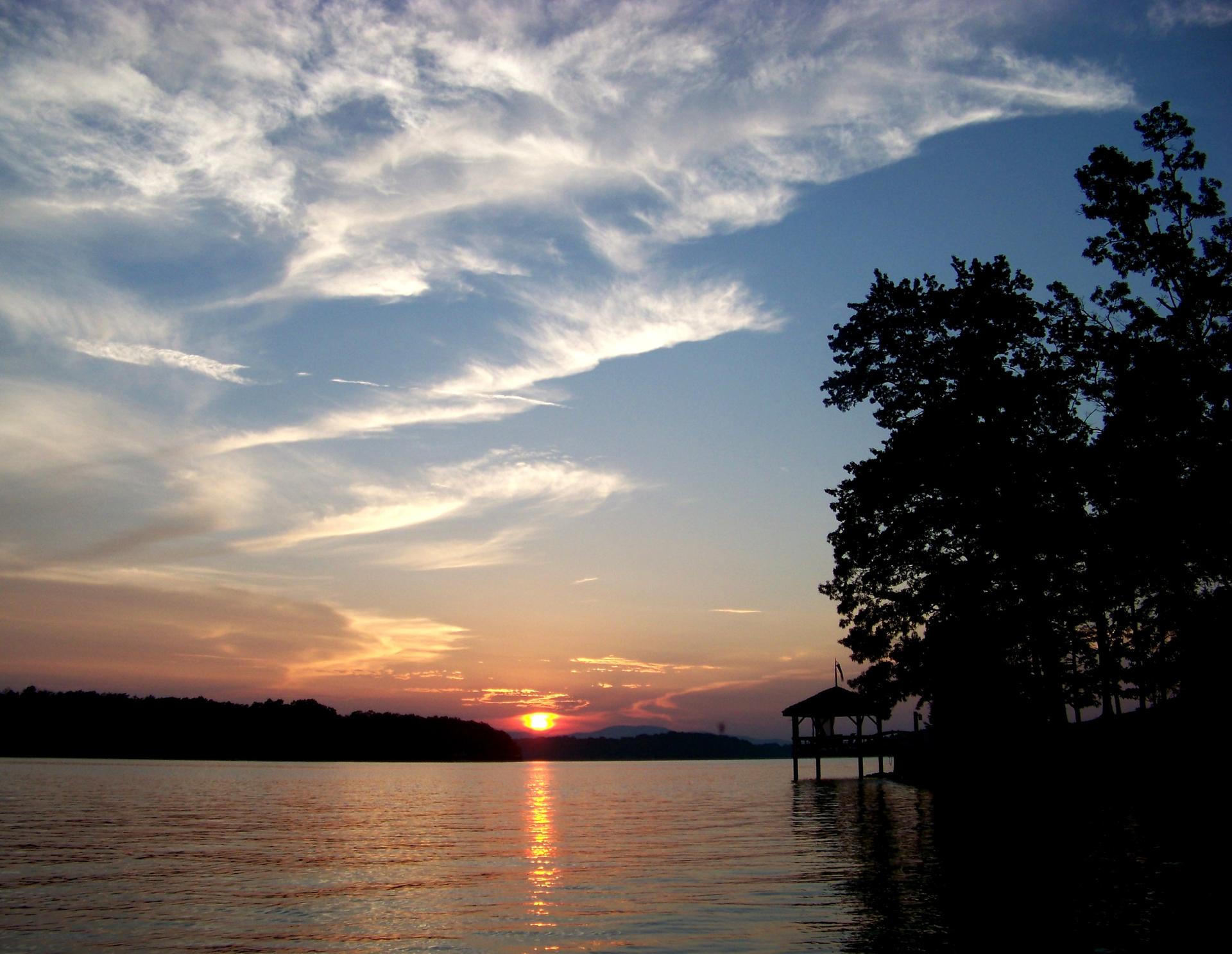 A vibrant sunset over a lake, with silhouetted trees and a dock.