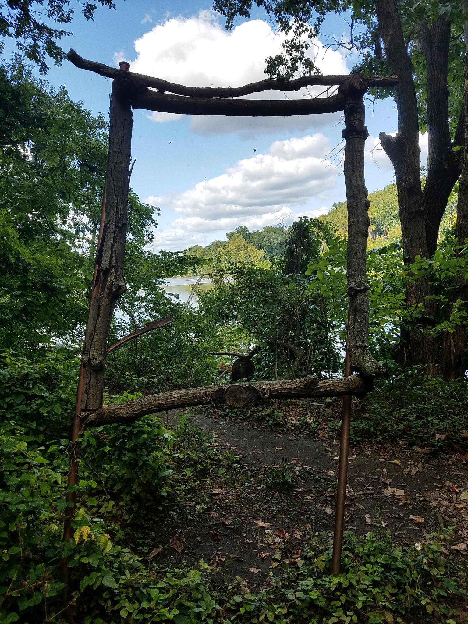 Rustic wooden archway frames a view of water and distant trees.
