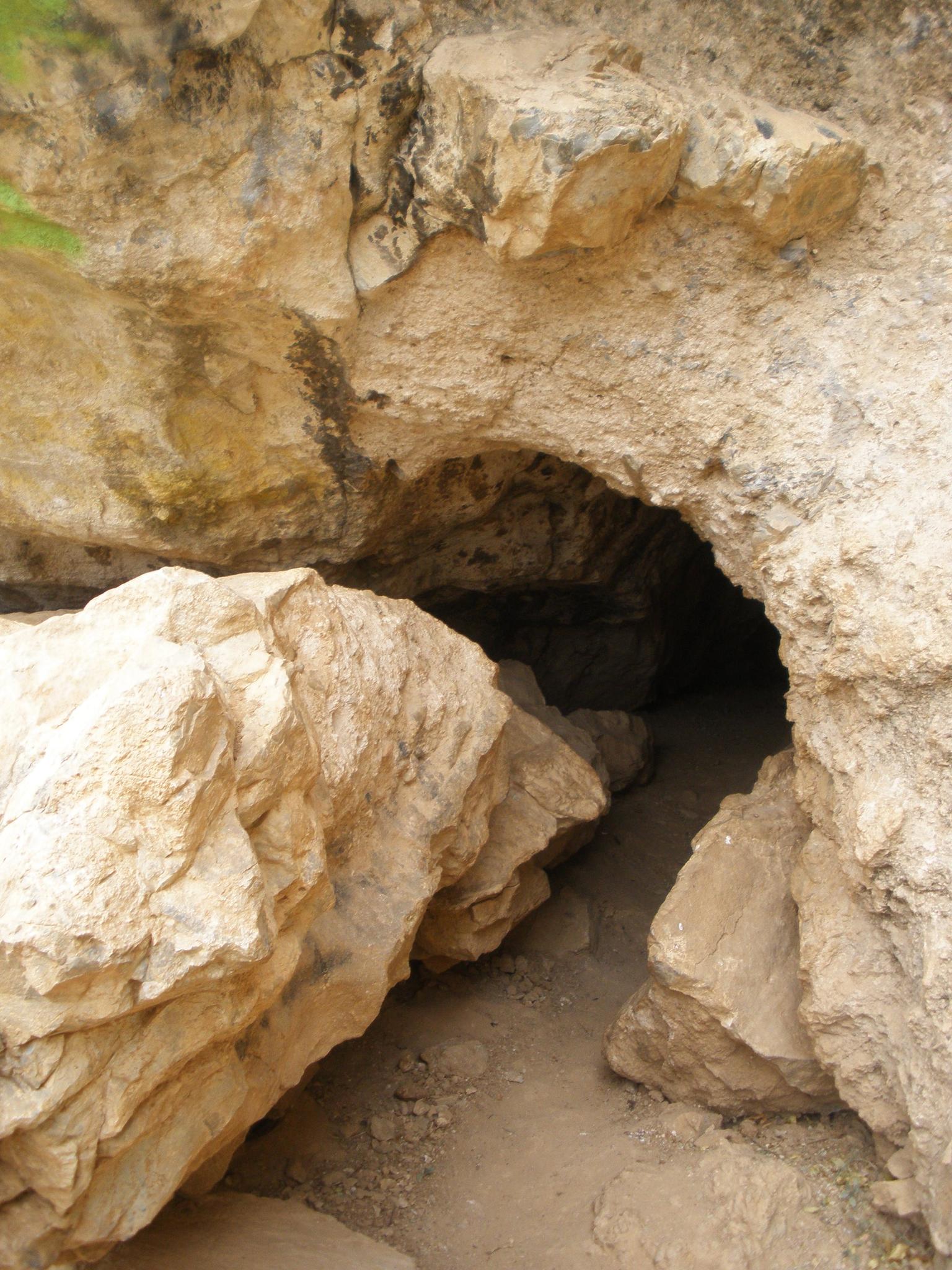Close-up of a dark cave entrance surrounded by large, light-colored rocks.