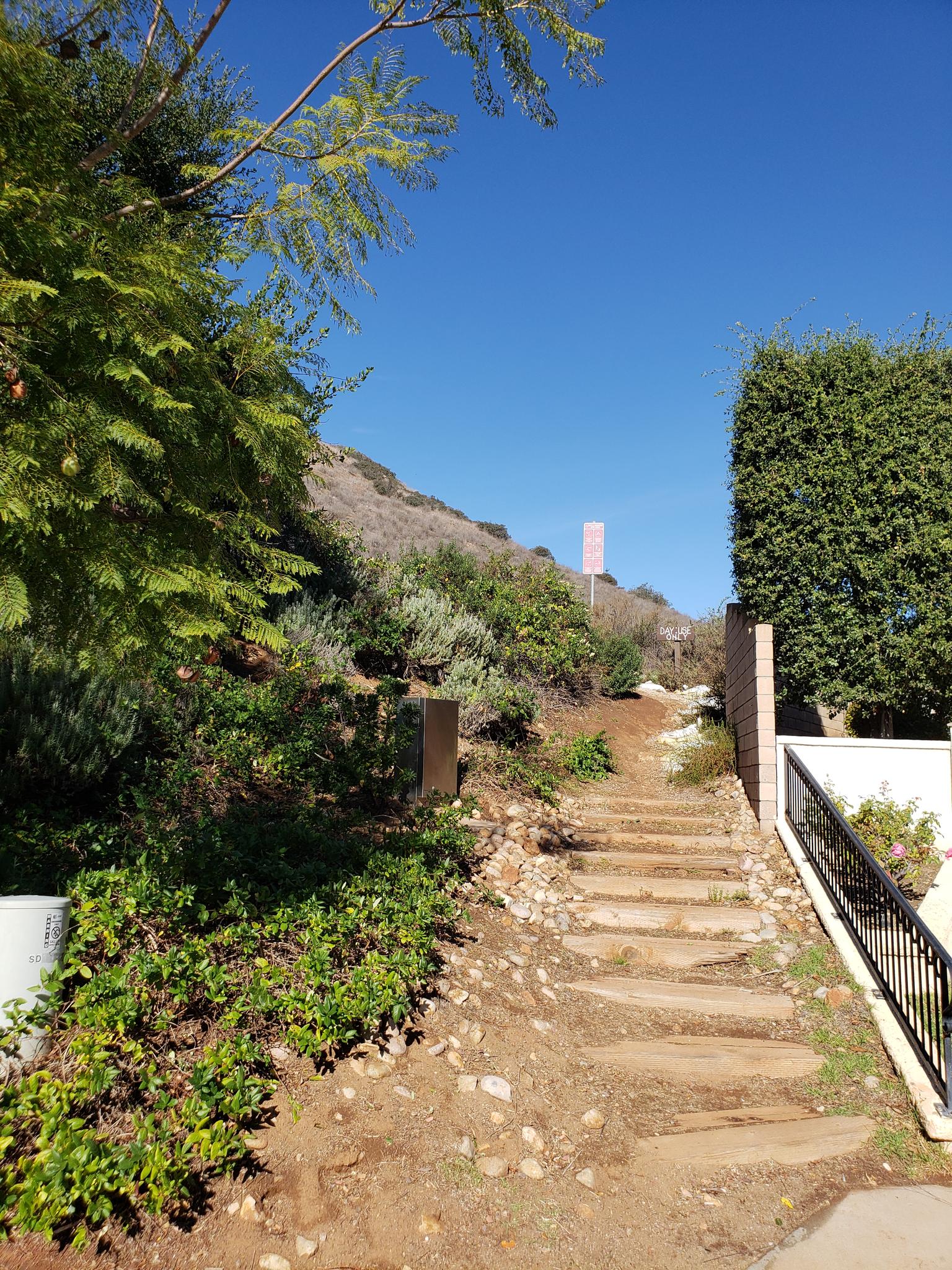 Stone steps ascend a dry, brushy hillside under a clear blue sky.