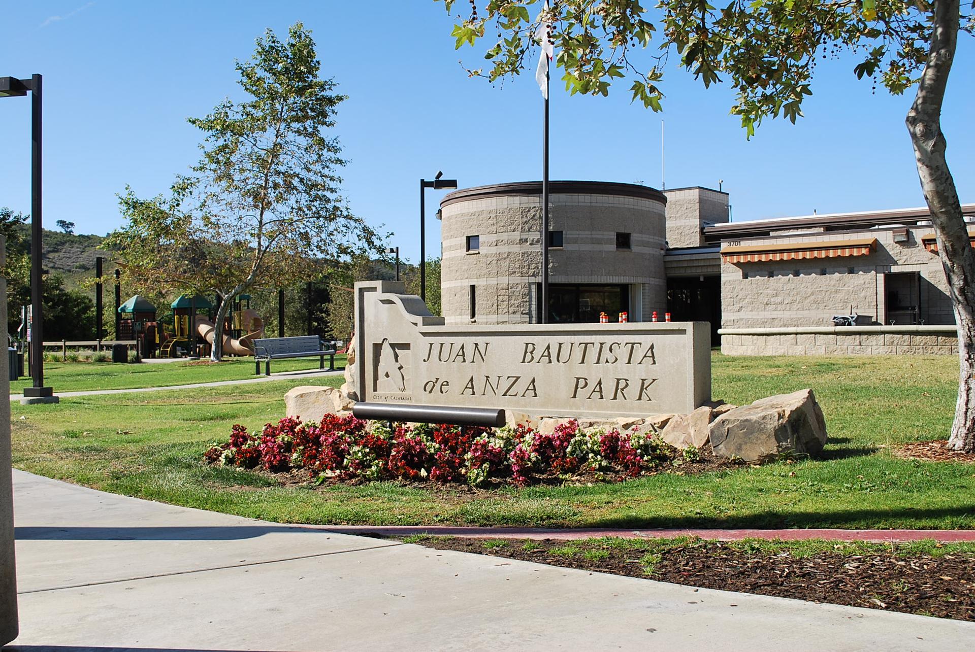 A large stone park sign with red flowers on a sunny day.