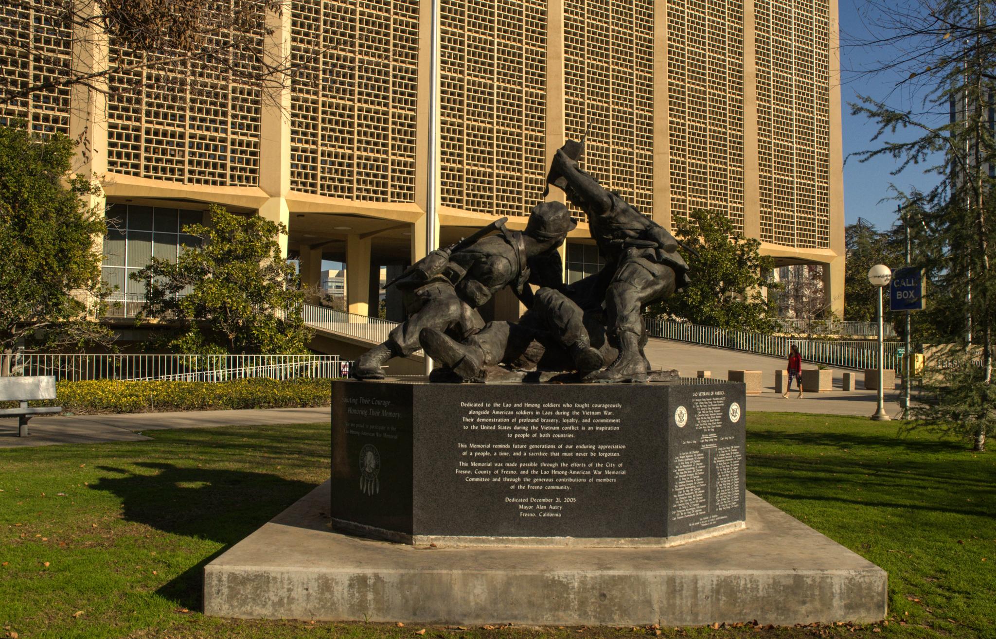 Bronze statue on a pedestal in front of a large building on a sunny day.