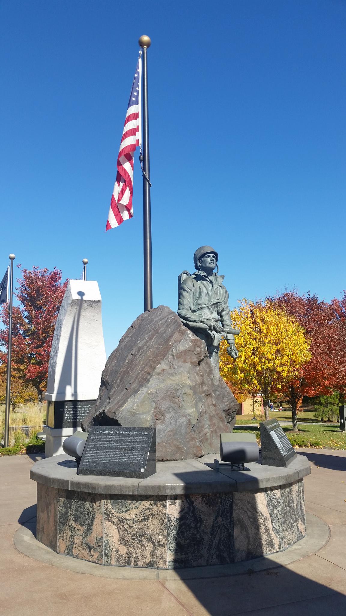 Bronze soldier statue, American flag, and monument on a sunny autumn day.