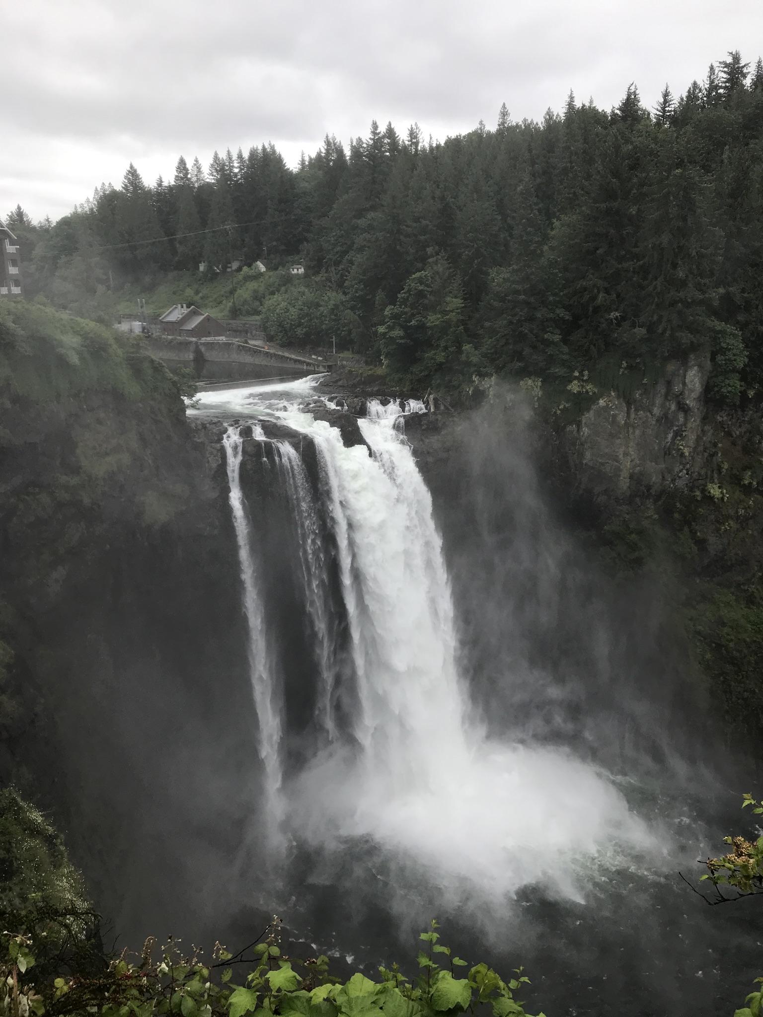 Overcast view of a powerful waterfall amidst misty, dark cliffs and forest.