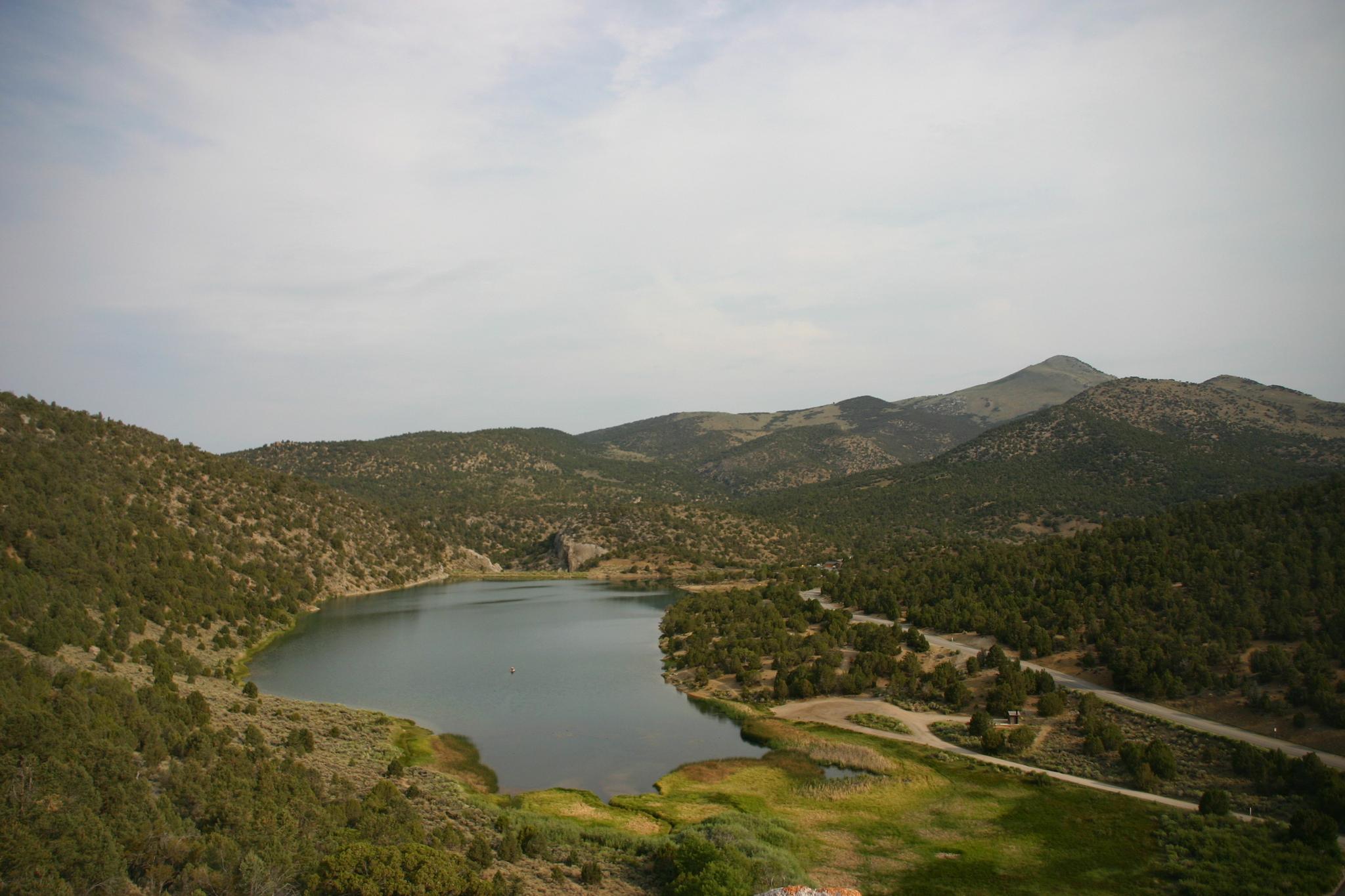 Overcast view of a serene lake nestled among green, tree-covered hills.
