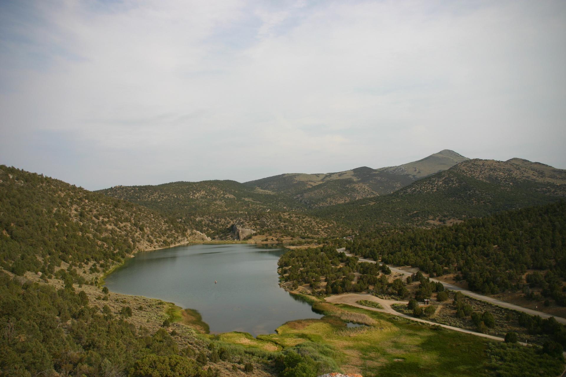 Overcast view of a serene lake nestled among green, tree-covered hills.