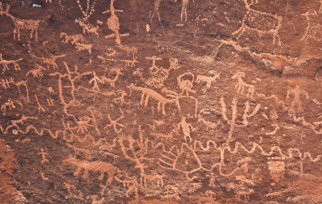 Numerous ancient petroglyphs depicting figures and animals carved into a rock face.