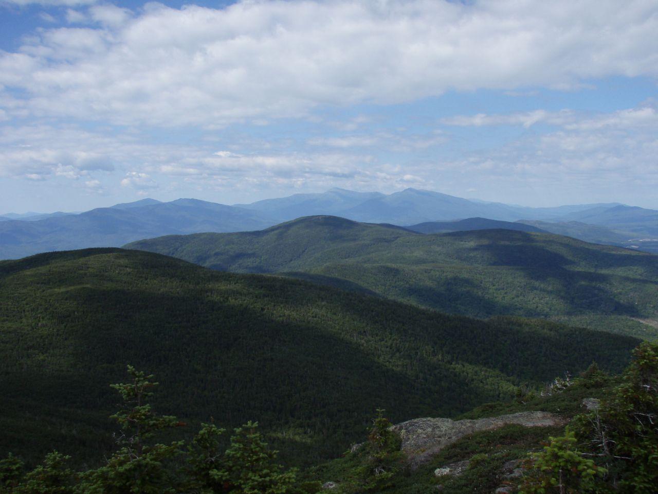 Vast mountain range with forested peaks under a cloudy sky.