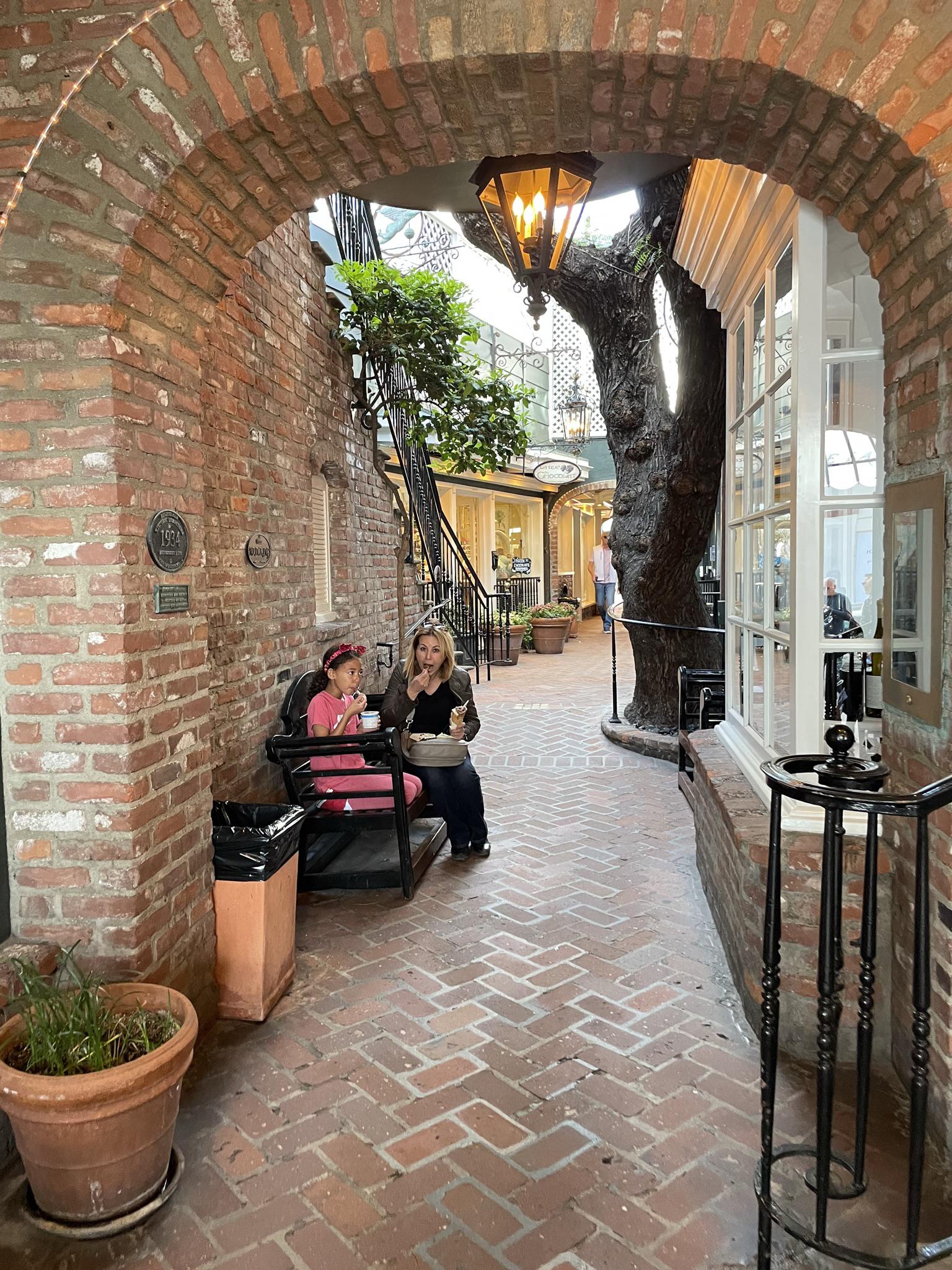 Two people sitting on a bench in a brick archway courtyard.