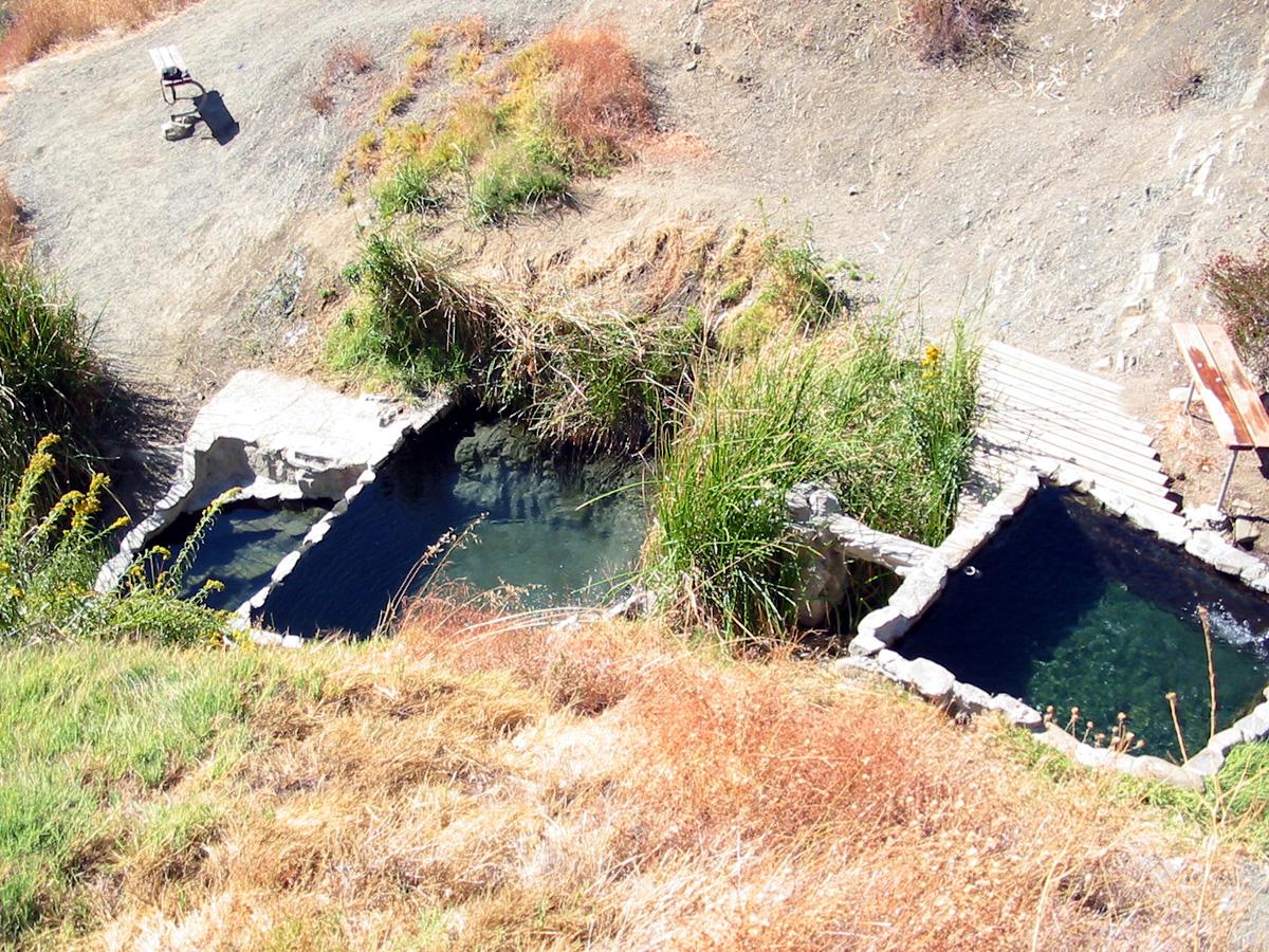 Three small, man-made pools on a dry, sunny, grassy slope.