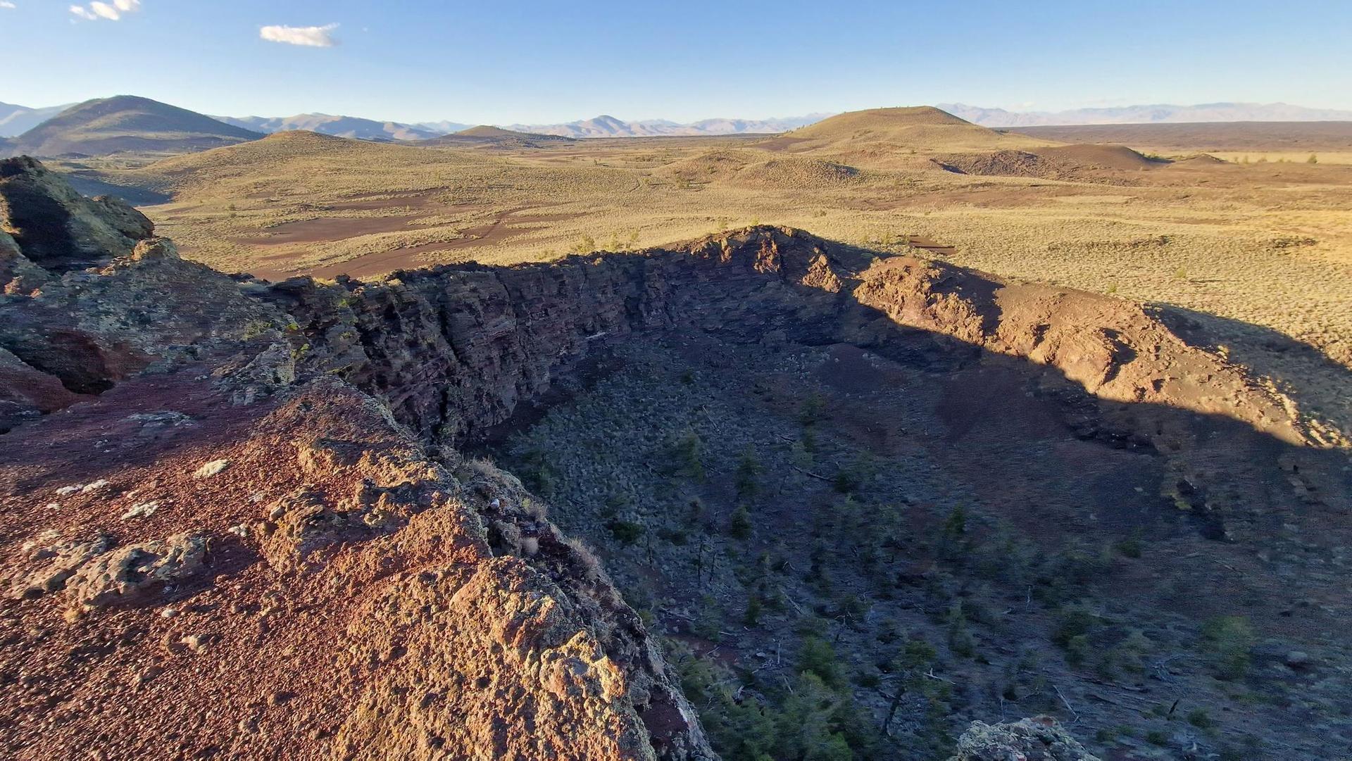 Aerial view of a large, rocky crater in a vast, arid landscape.