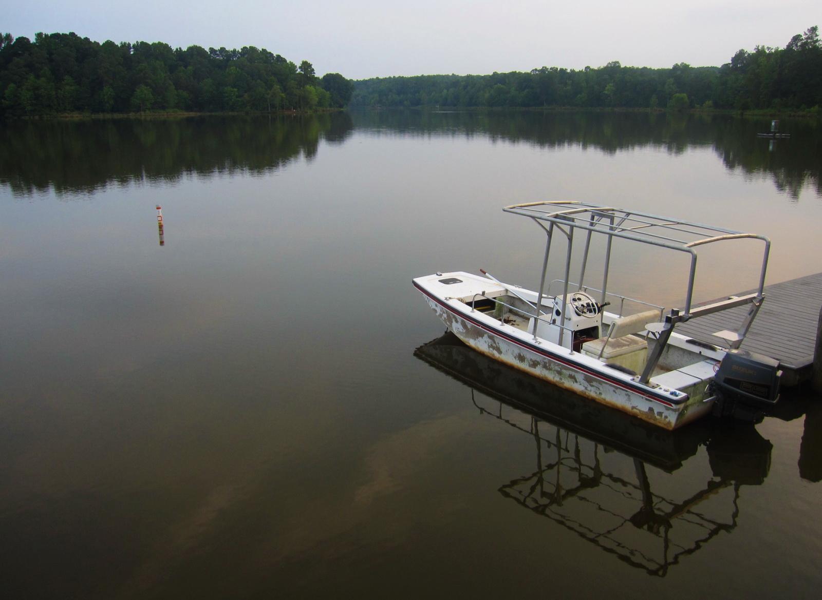 A boat docked on a calm lake with a person fishing in the distance.