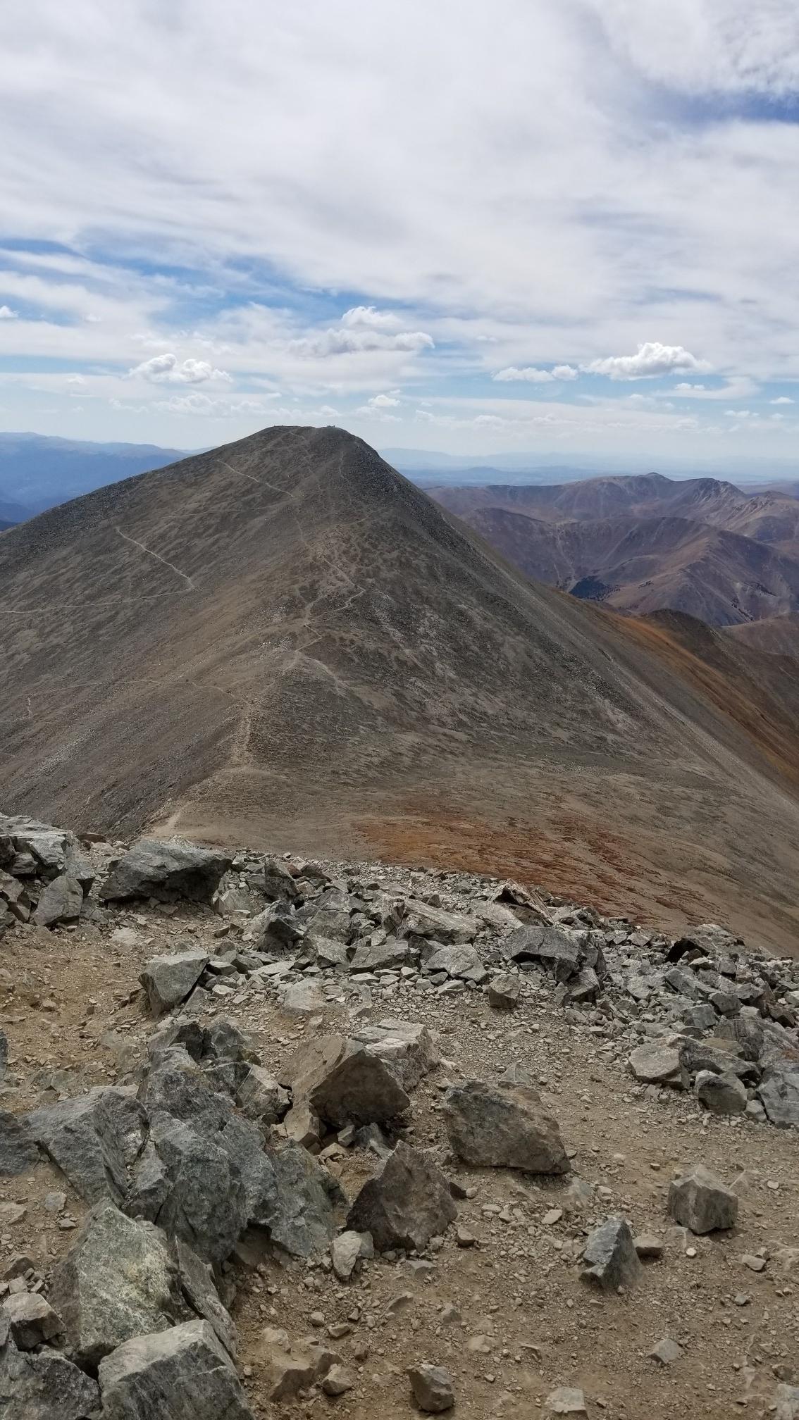 A winding path ascends a barren mountain ridge under a cloudy sky.