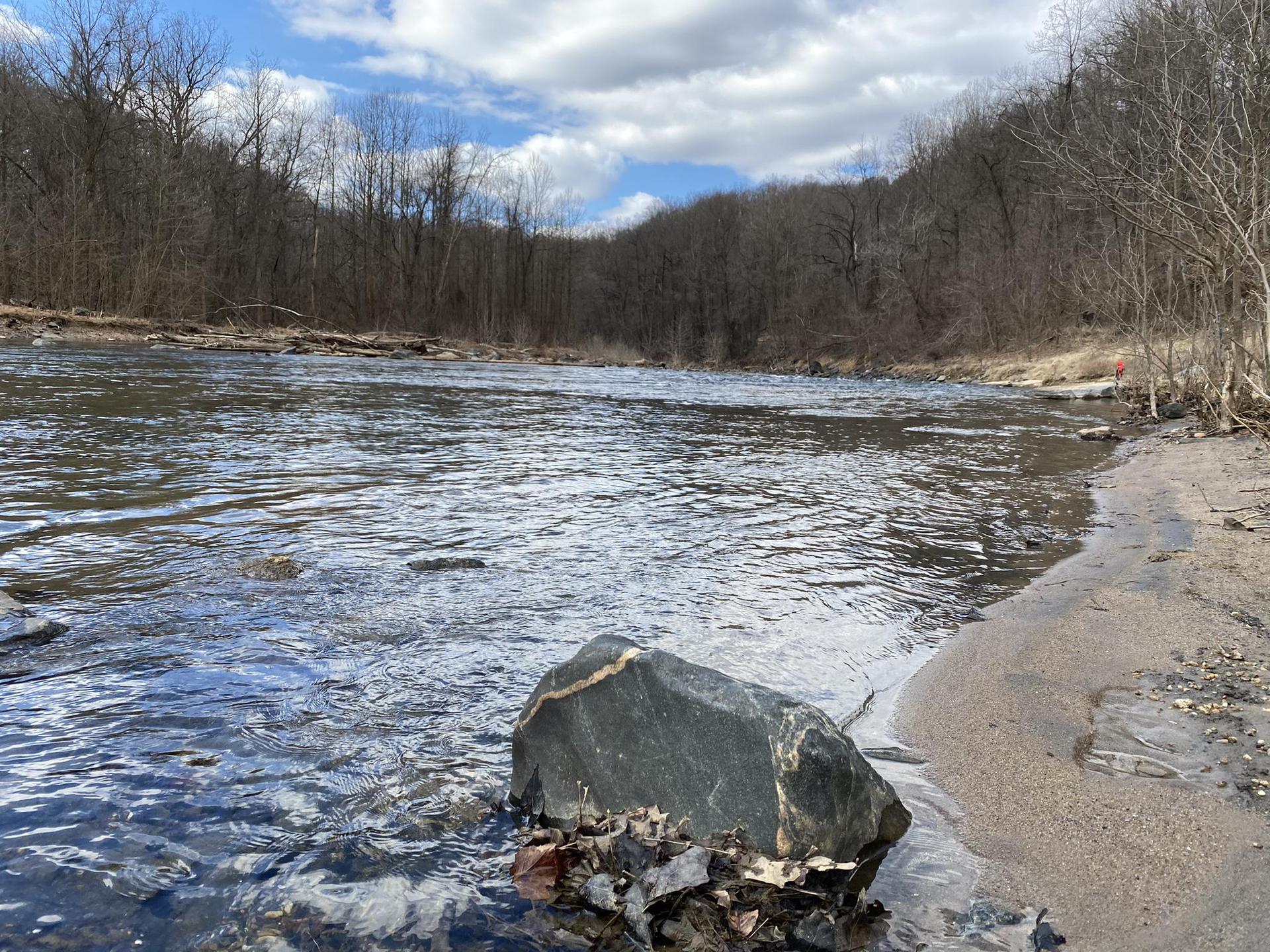 A wide river with a large rock on a sandy bank under a cloudy sky.