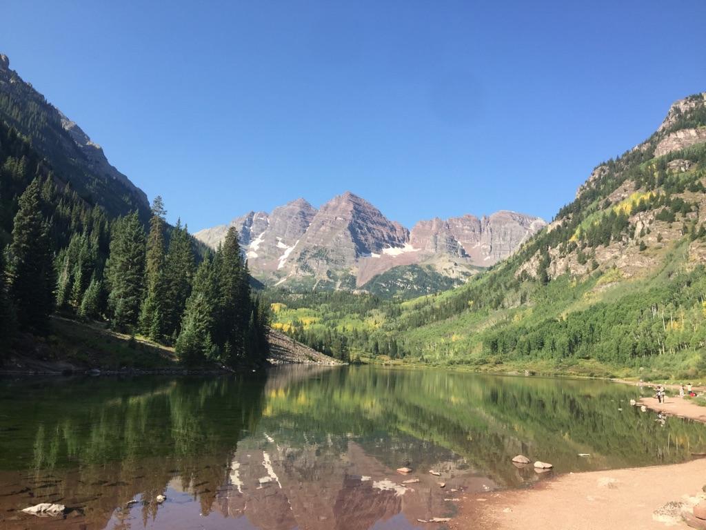 Bright sunny day over a calm lake reflecting mountains and green trees.