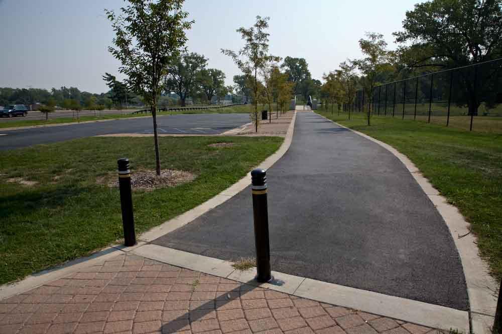 Sunny view of a paved walking path next to green grass and trees.