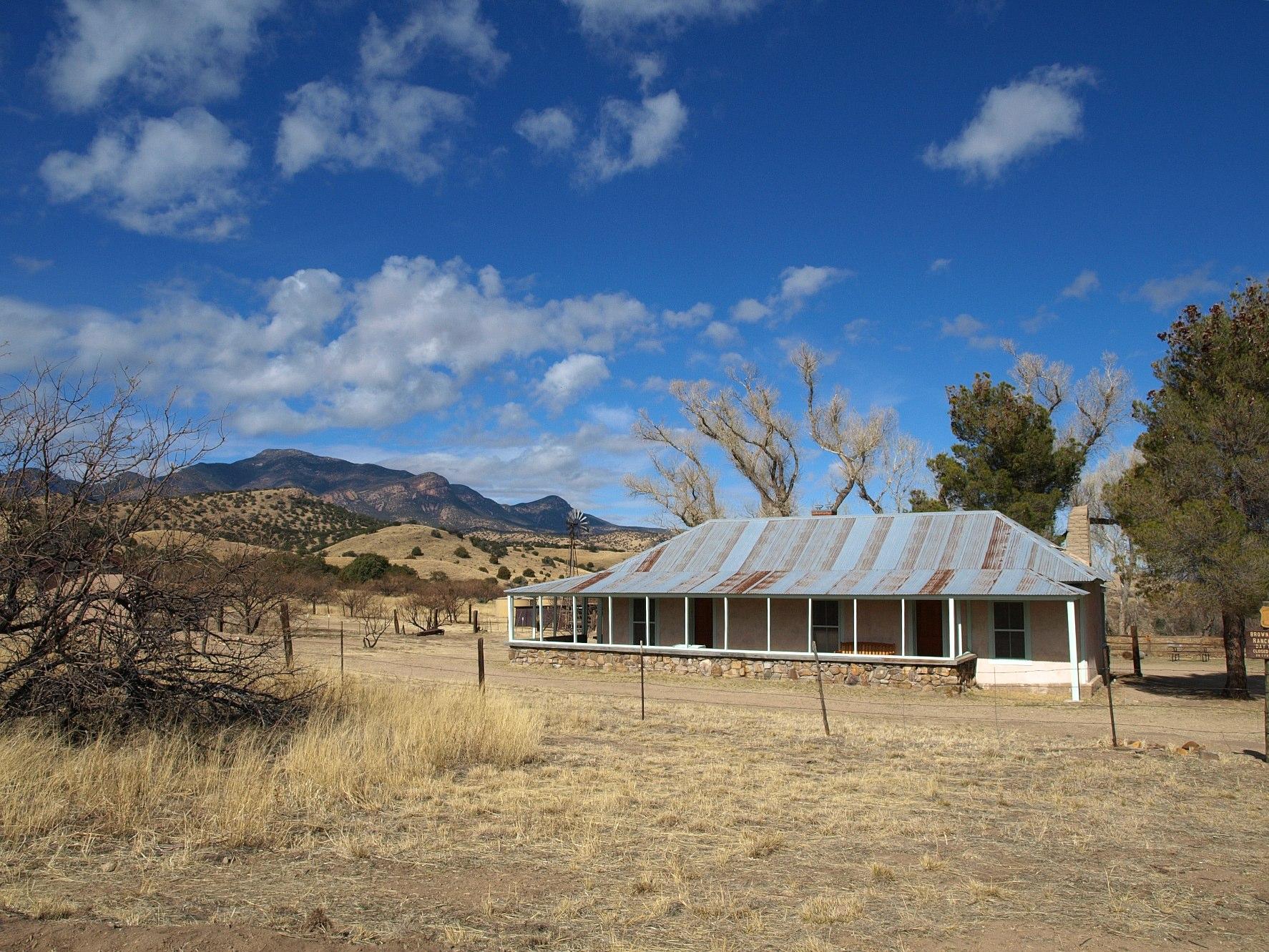 An old house with a metal roof sits in a dry, sunny landscape.