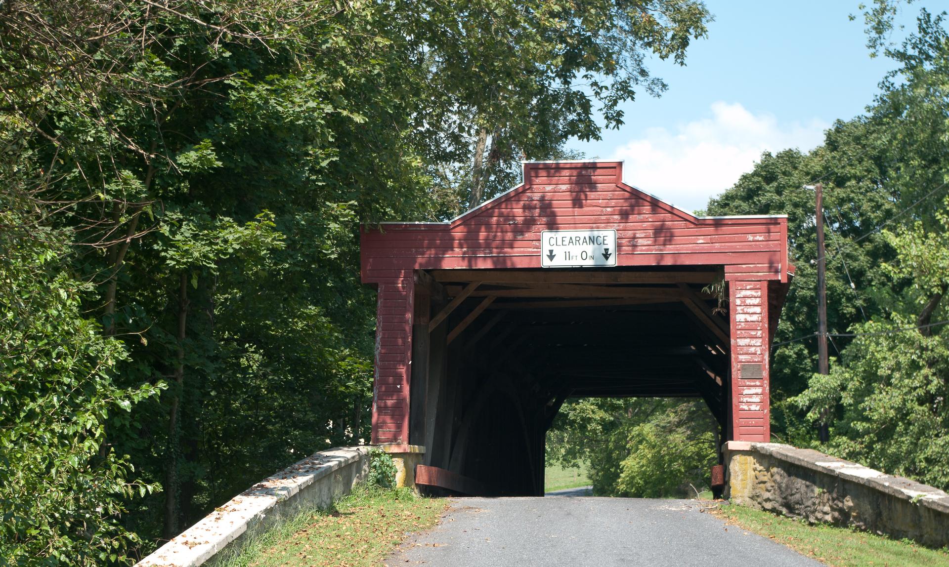 Historic red covered bridge surrounded by dense green summer foliage.