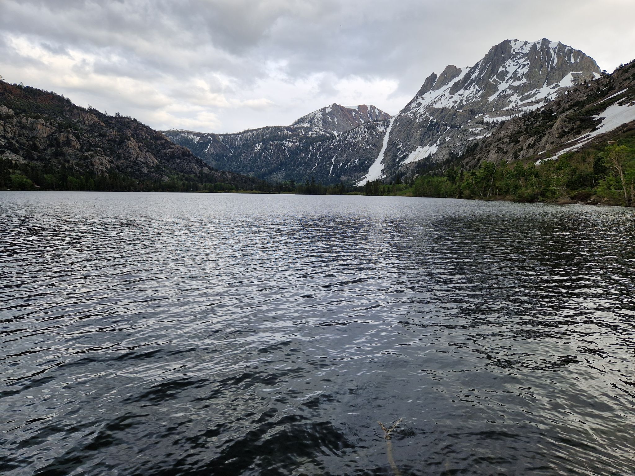 A dark lake with snow-capped mountains and green trees under a cloudy sky. - Silver Lake Loop Trail