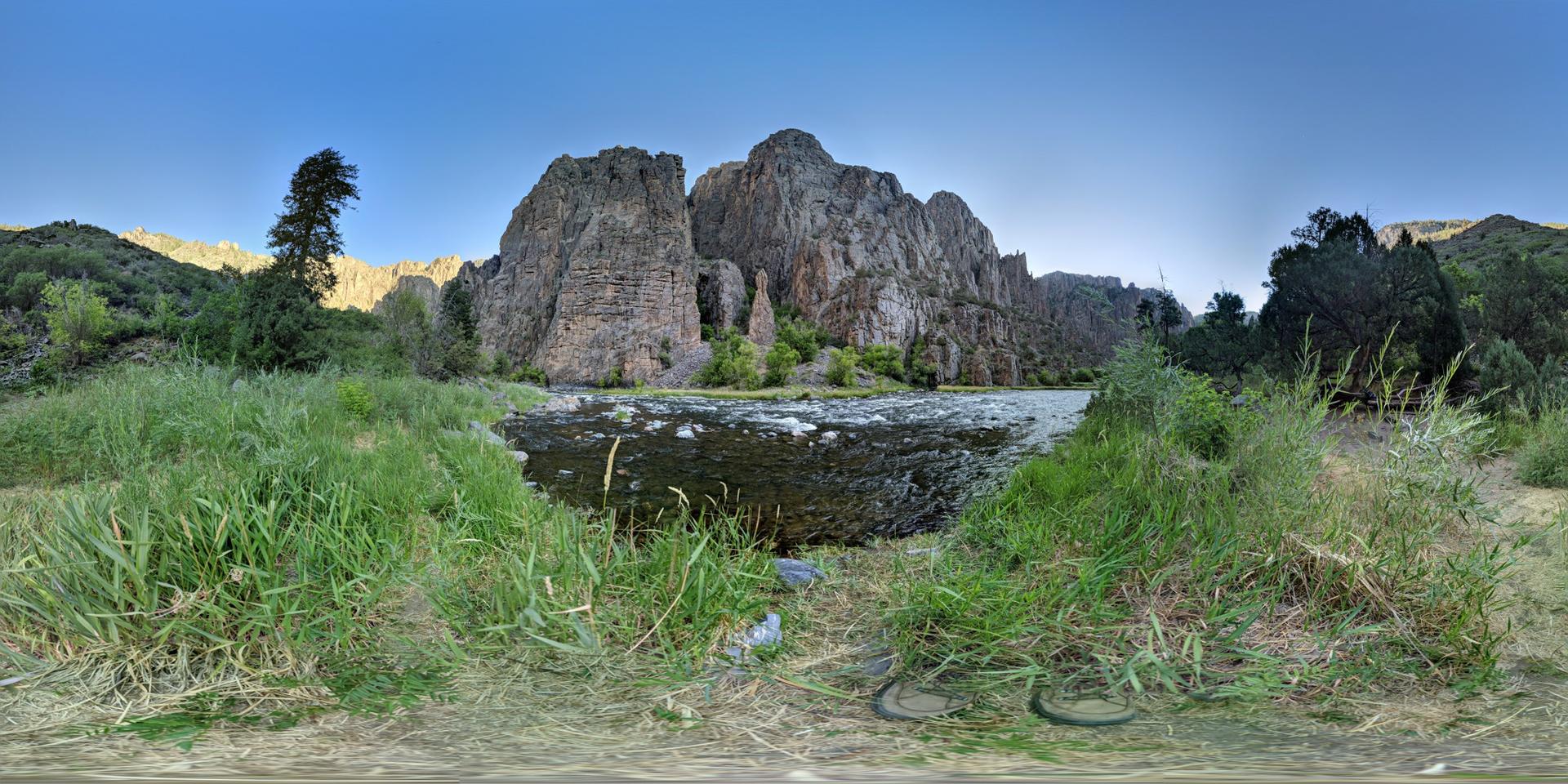 Panoramic view of a river flowing past towering rock formations and green banks.